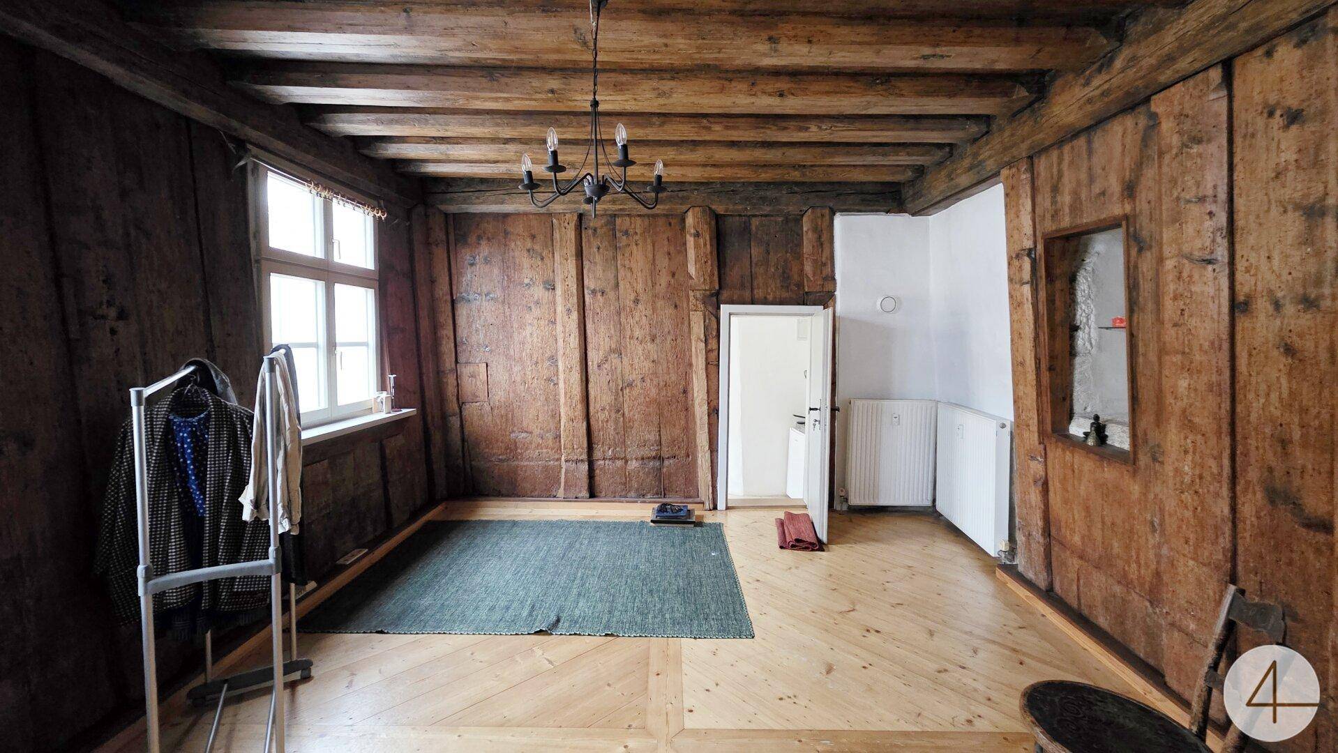 Zimmer mit rustikalen Holzvertäfelungen an Wänden und Decke sowie hellem Holzboden und Fenstern.