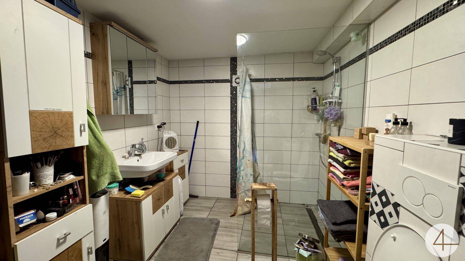 Funktionales Badezimmer mit Fliesen, Duschkabine und Waschbecken mit Spiegelschrank.