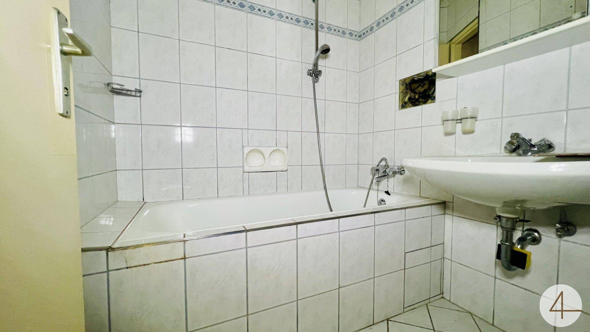 Gefliestes Badezimmer mit Badewanne und Waschbecken, im älteren Stil gehalten.