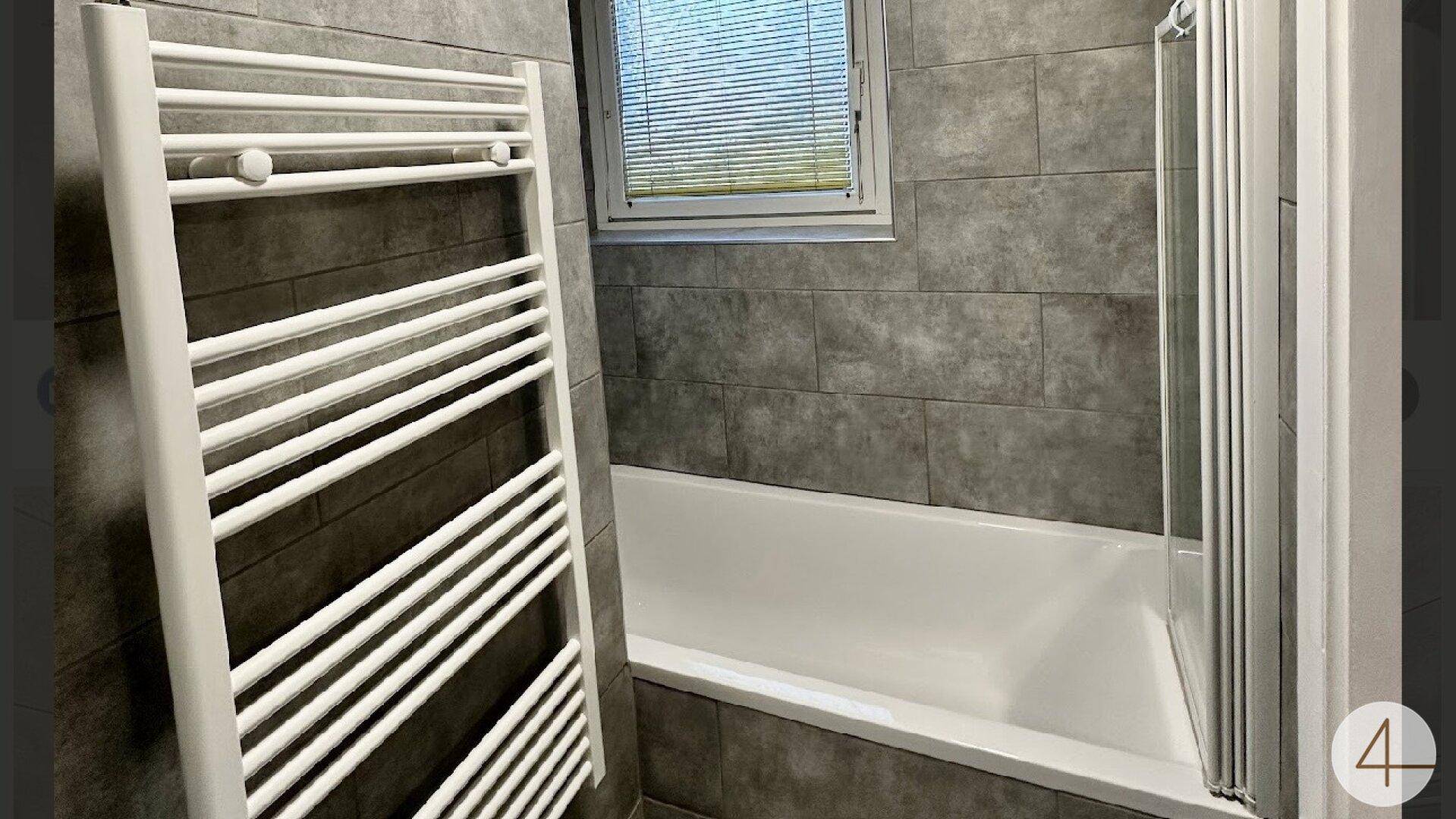 Modernes Badezimmer mit grauen Fliesen, Badewanne und beheiztem Handtuchhalter.