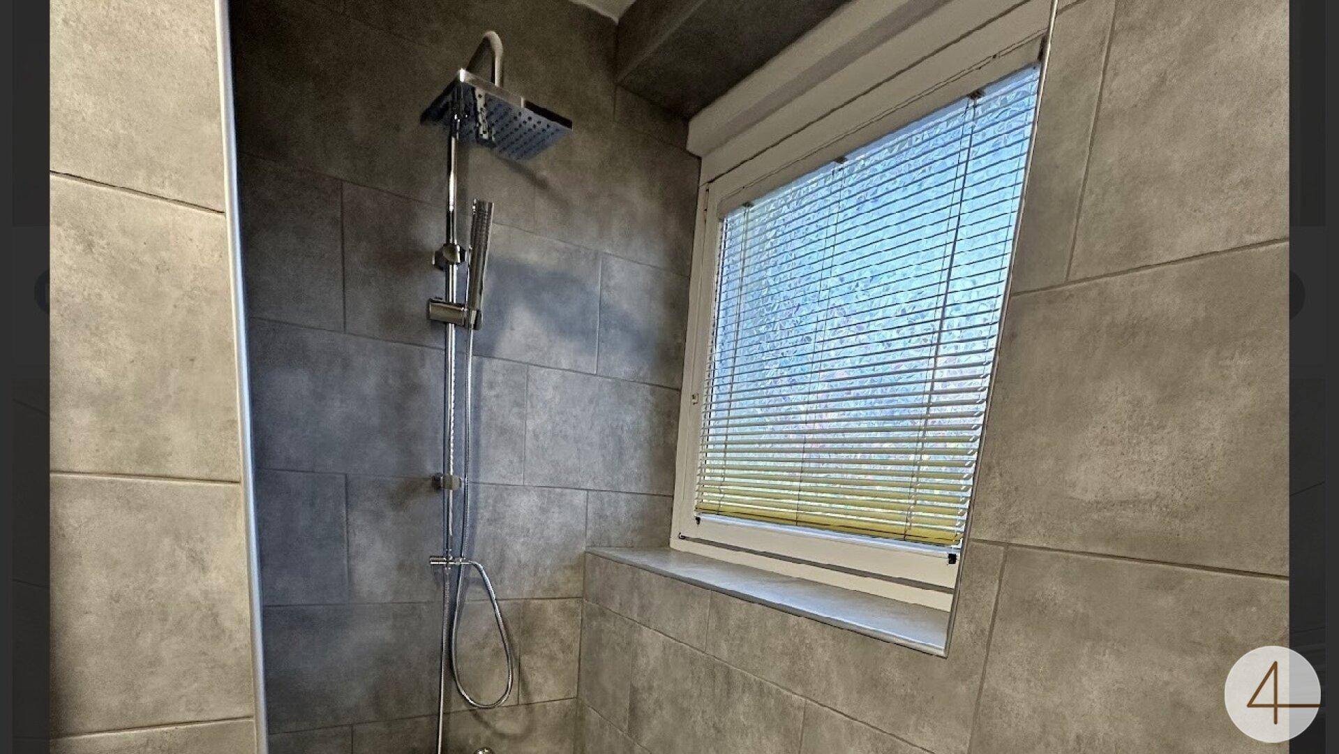 Duschbereich im Badezimmer mit Regendusche und Fenster mit Jalousien.