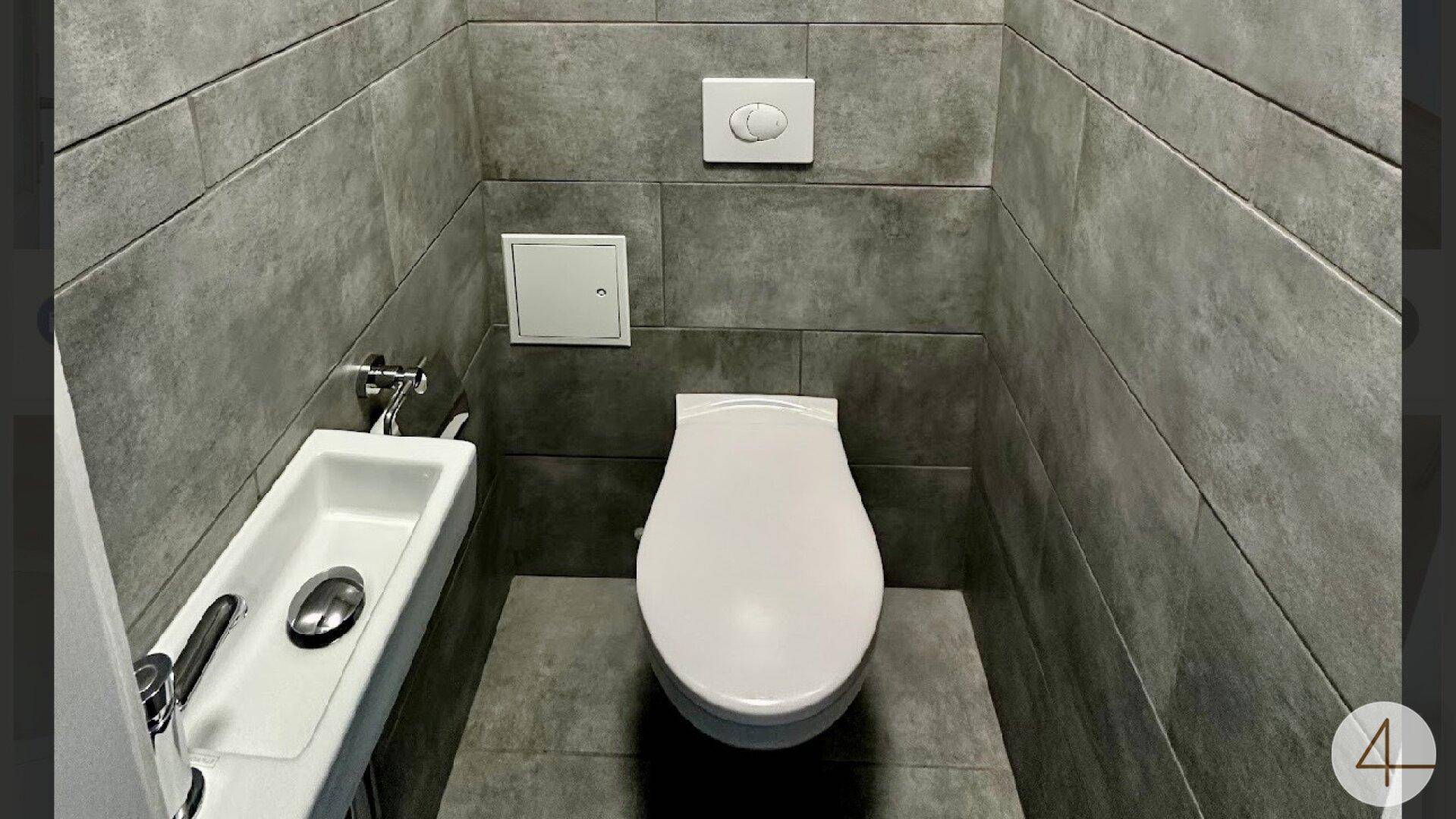 Kleines Gäste-WC mit Wand-WC, kleinem Waschbecken und grauen Wandfliesen.