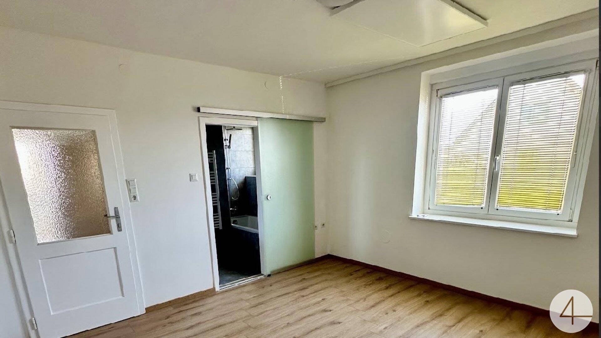 Helles Zimmer mit Laminatboden und Schiebetür zum angrenzenden Badezimmer.