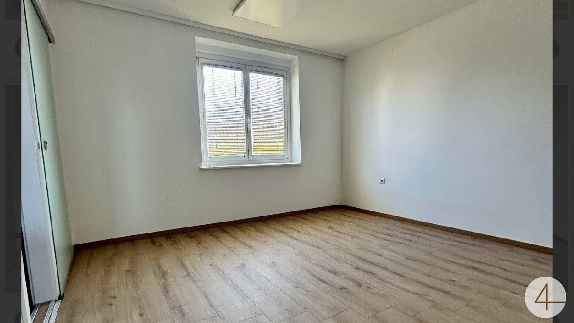 Geräumiges Zimmer mit Laminatboden und großem Fenster, das viel Tageslicht hereinlässt.