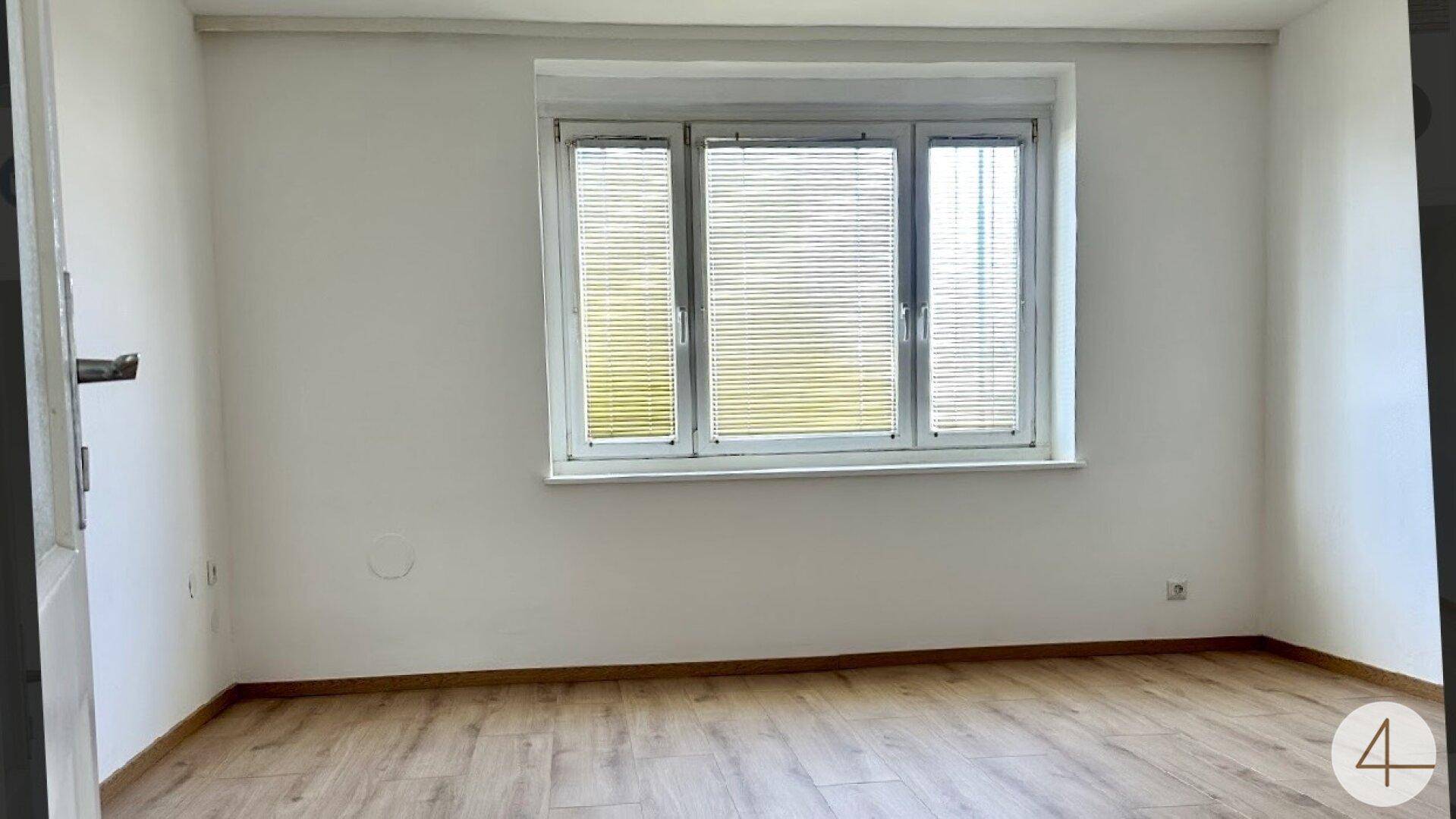 Helles Zimmer mit großem Fenster und Laminatboden, bietet viel natürliches Licht.
