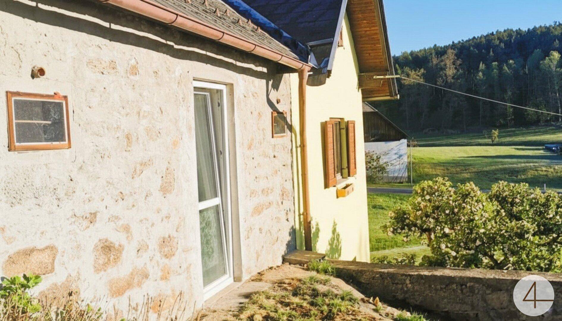 Seitenansicht eines Hauses mit Steinfassade und Blick auf die umliegende Landschaft.