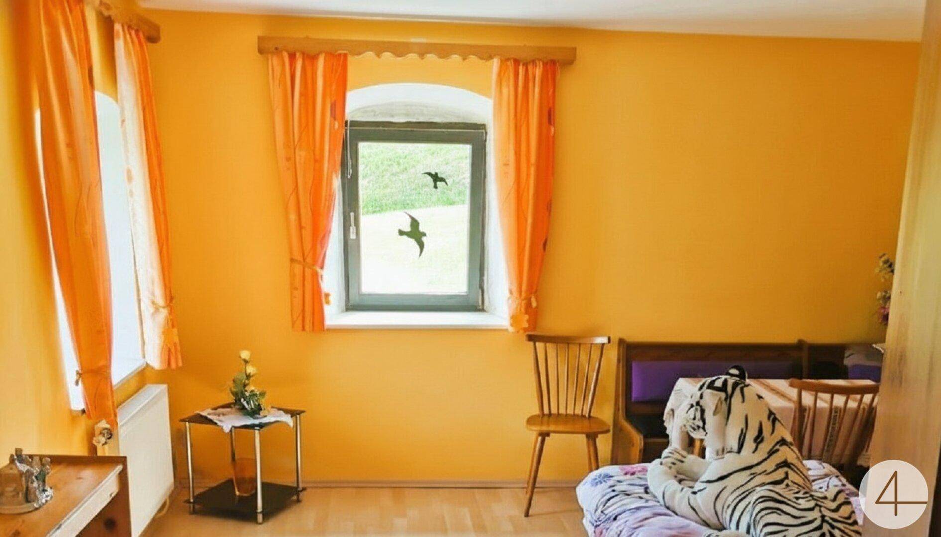 Helles Schlafzimmer mit orangefarbenen Wänden, Fenster und traditioneller Einrichtung.