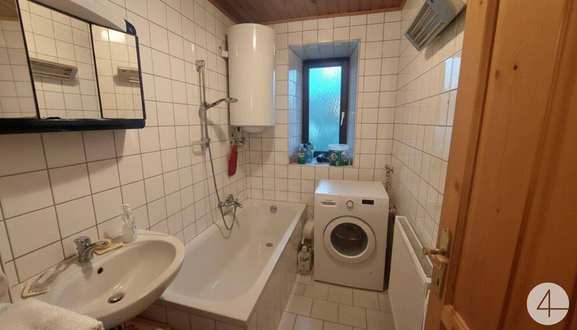 Helles Badezimmer mit Badewanne, Waschmaschine und weißen Fliesen.