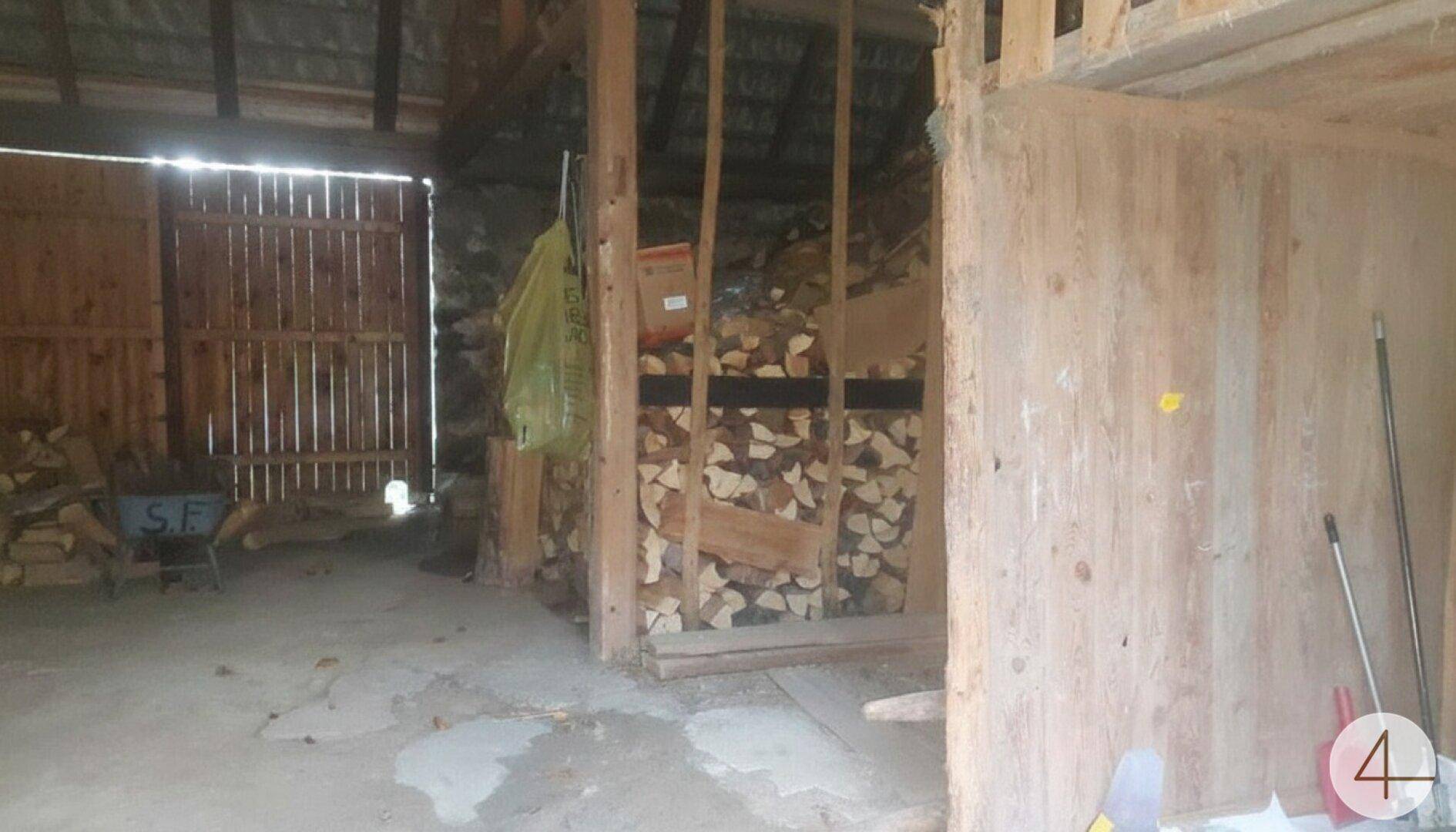 Lagerraum für Brennholz mit gestapelten Holzscheiten und einfacher Holzkonstruktion.
