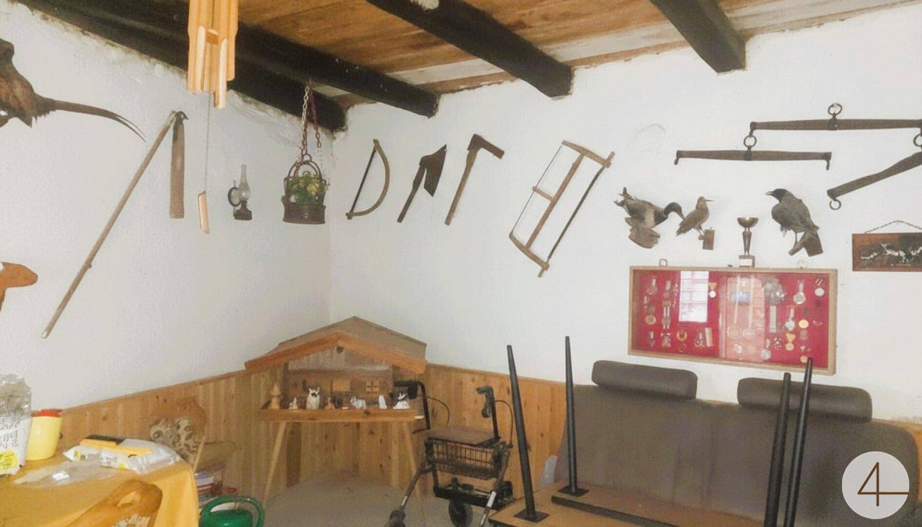 Rustikaler Raum mit Holzbalkendecke und einer Sammlung traditioneller Werkzeuge und Dekorationen.