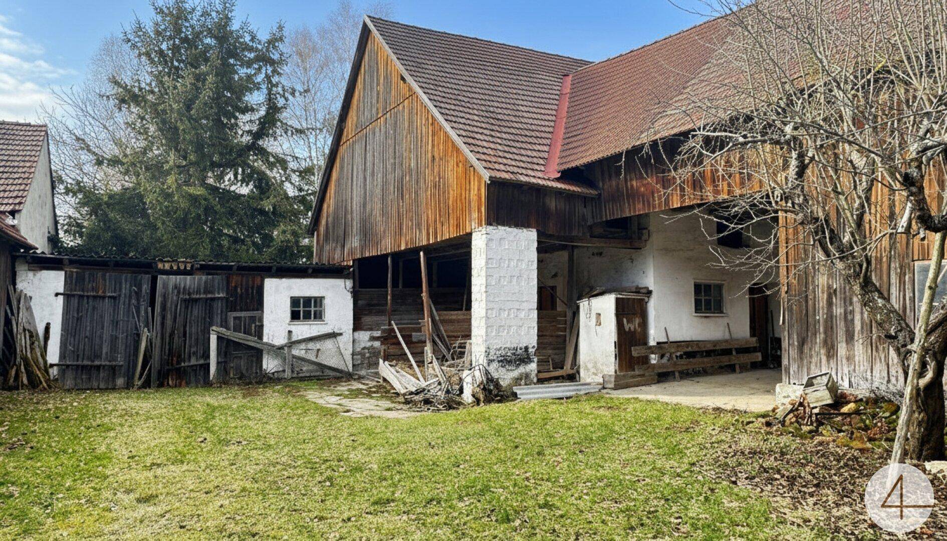 Rustikaler Bauernhof mit Holzfassade und großem Gartenbereich unter klarem Himmel.