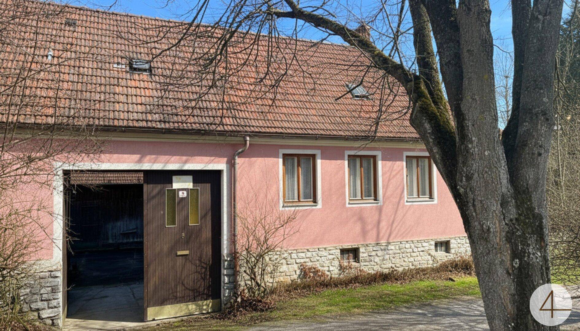 Haus mit rosafarbener Fassade, Steinsockel und großem Garagentor.