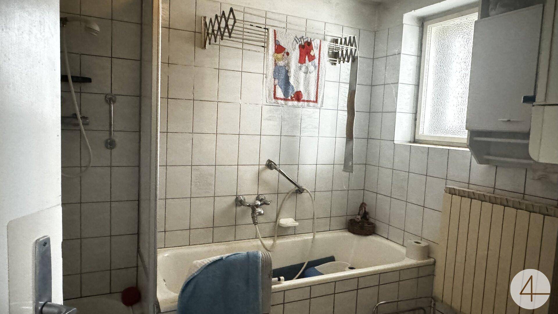 Badezimmer mit weißen Fliesen, Badewanne und Fenster, ausgestattet mit einem Heizkörper.