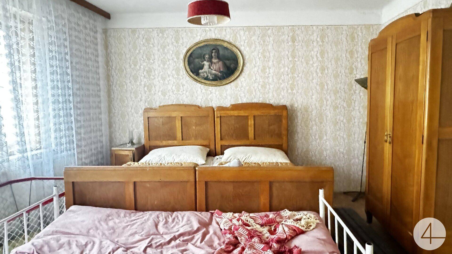 Schlafzimmer mit zwei Einzelbetten, Holzmöbeln und gemusterter Tapete in traditionellem Stil.