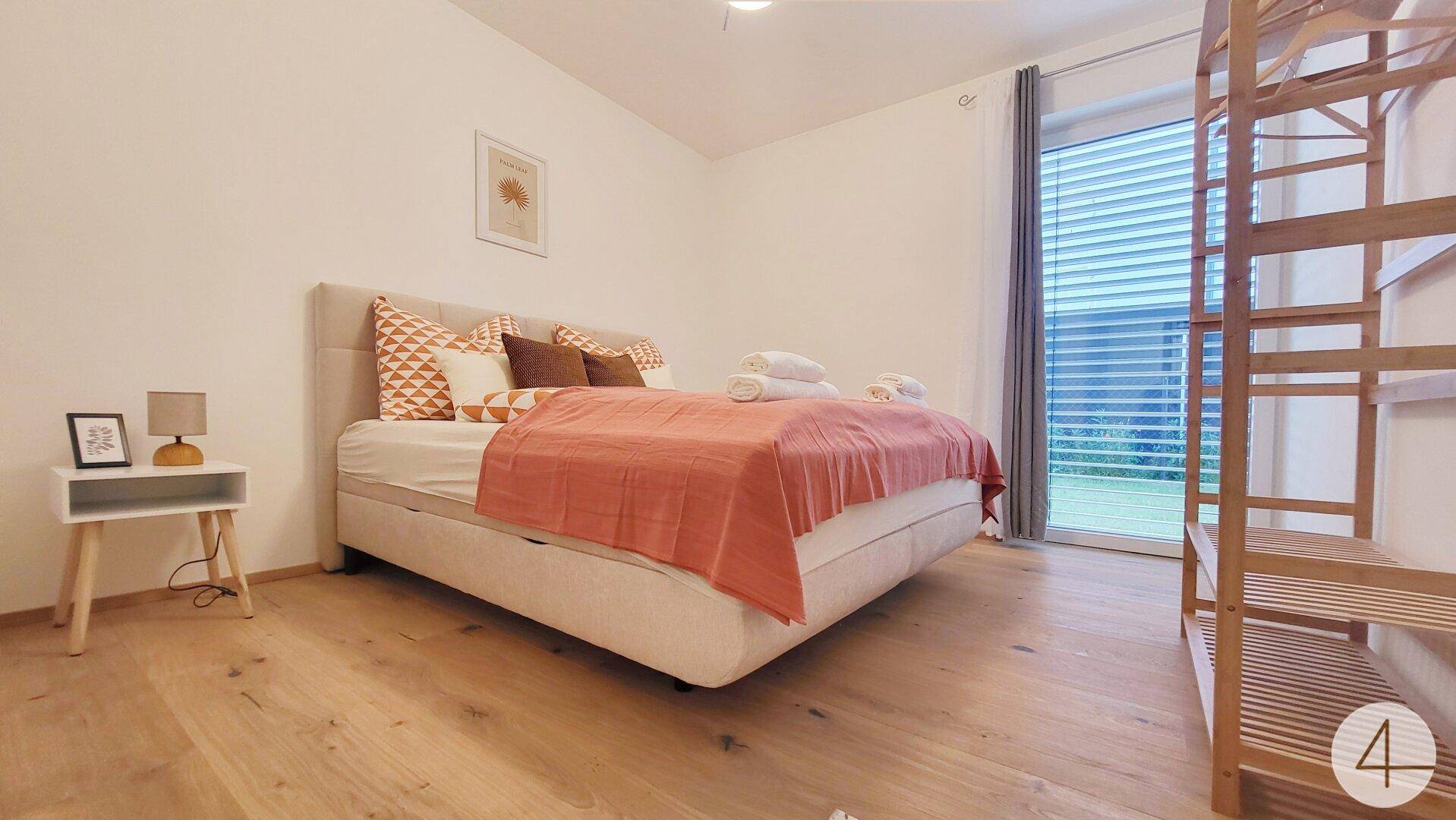 Helles Schlafzimmer mit Holzboden, großem Bett und direktem Zugang zum Garten.