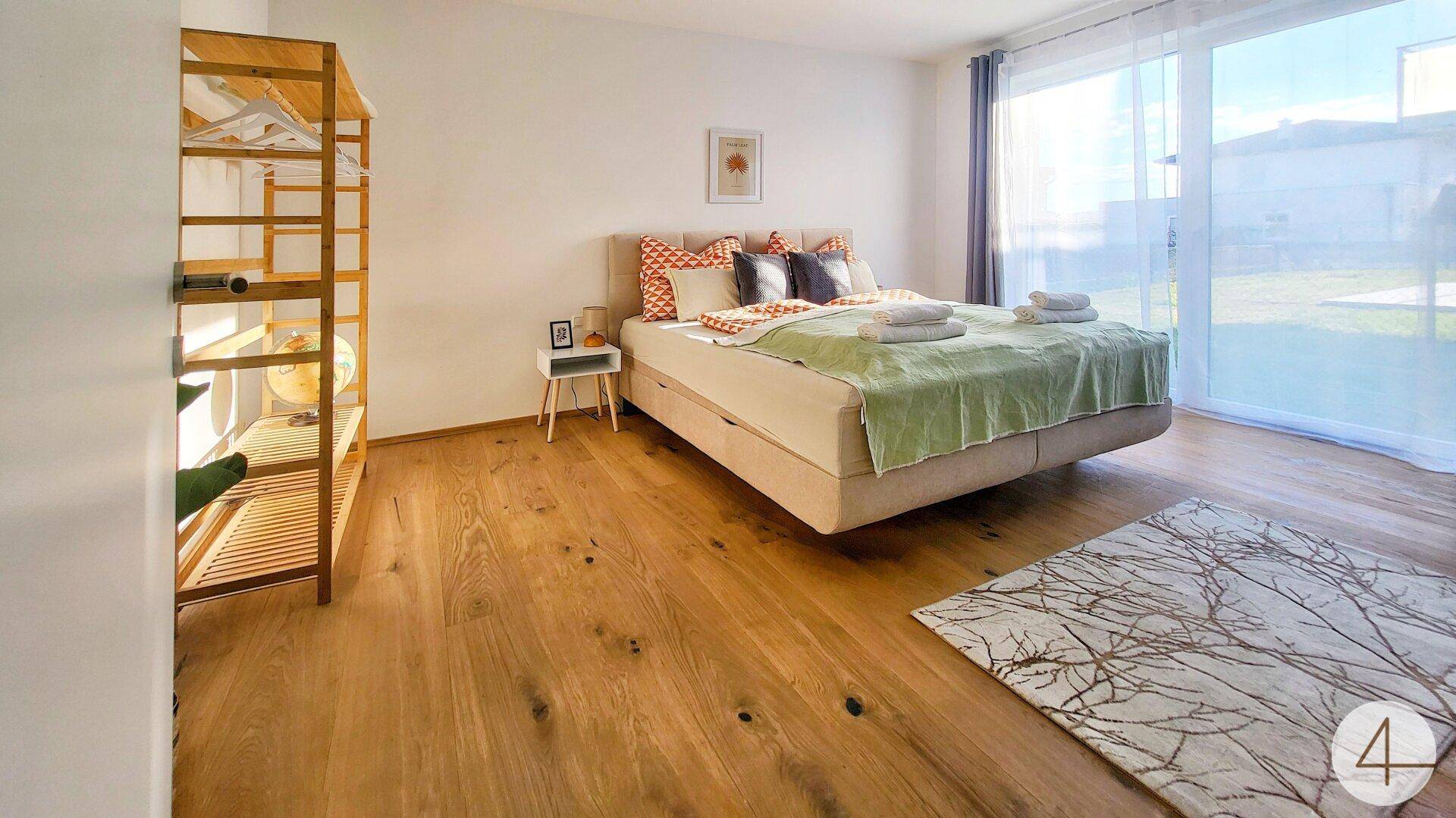 Geräumiges Schlafzimmer mit Holzboden, Doppelbett und viel Tageslicht durch große Fenster.