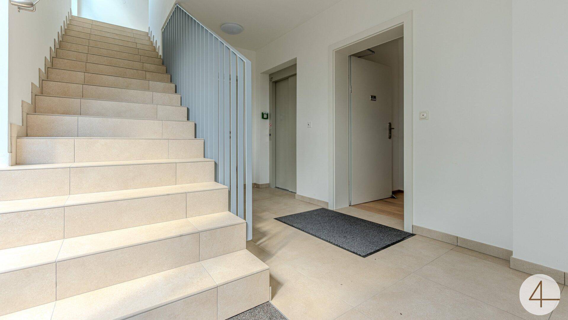 Treppenhaus und Aufzug in einem modernen Gebäude mit hellem Fliesenboden.