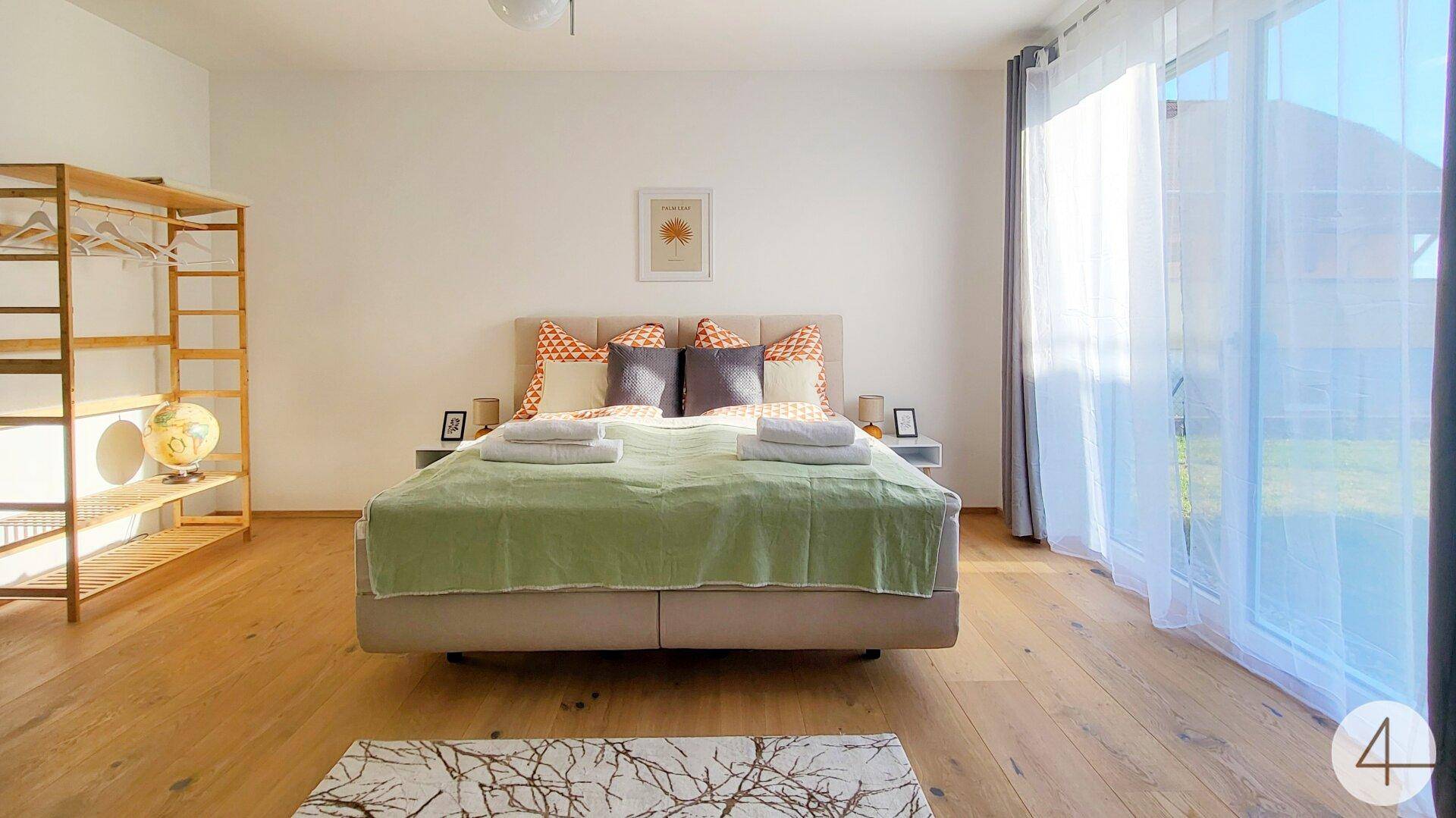 Geräumiges Schlafzimmer mit Holzboden, Doppelbett und viel Tageslicht durch große Fenster.