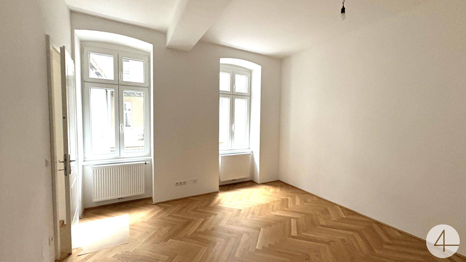 Geräumiges Schlafzimmer mit Fischgrätparkett und hohen Fenstern, die für viel Tageslicht sorgen.