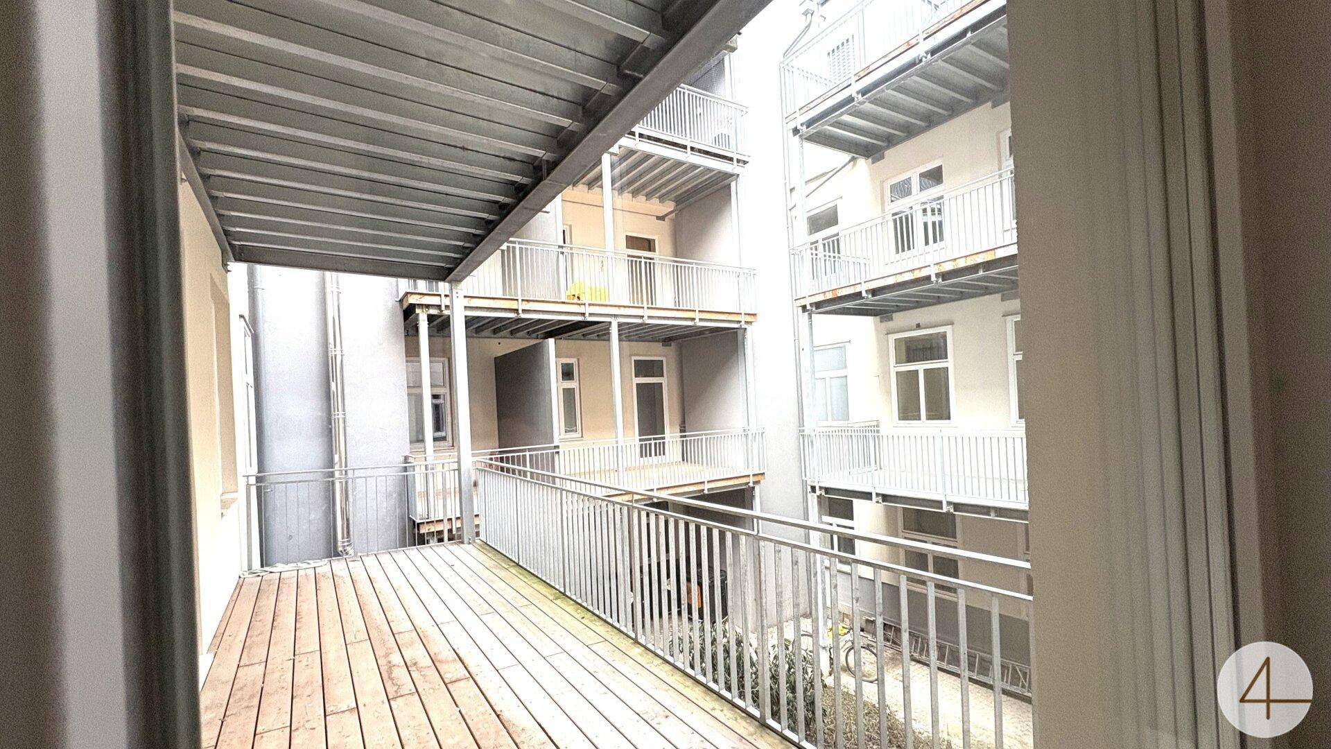 Großer Balkon mit Holzboden und Metallgeländer, der einen Blick auf den Innenhof bietet.