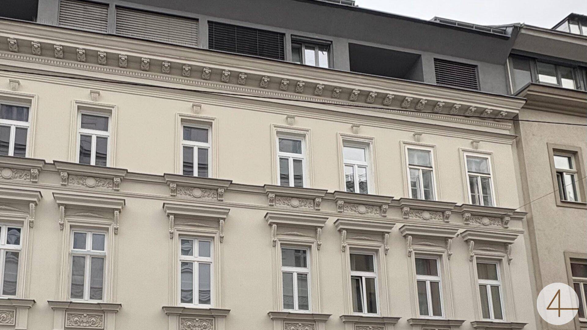 Klassische Fassade eines Altbaus mit vielen Fenstern und dekorativen Elementen.