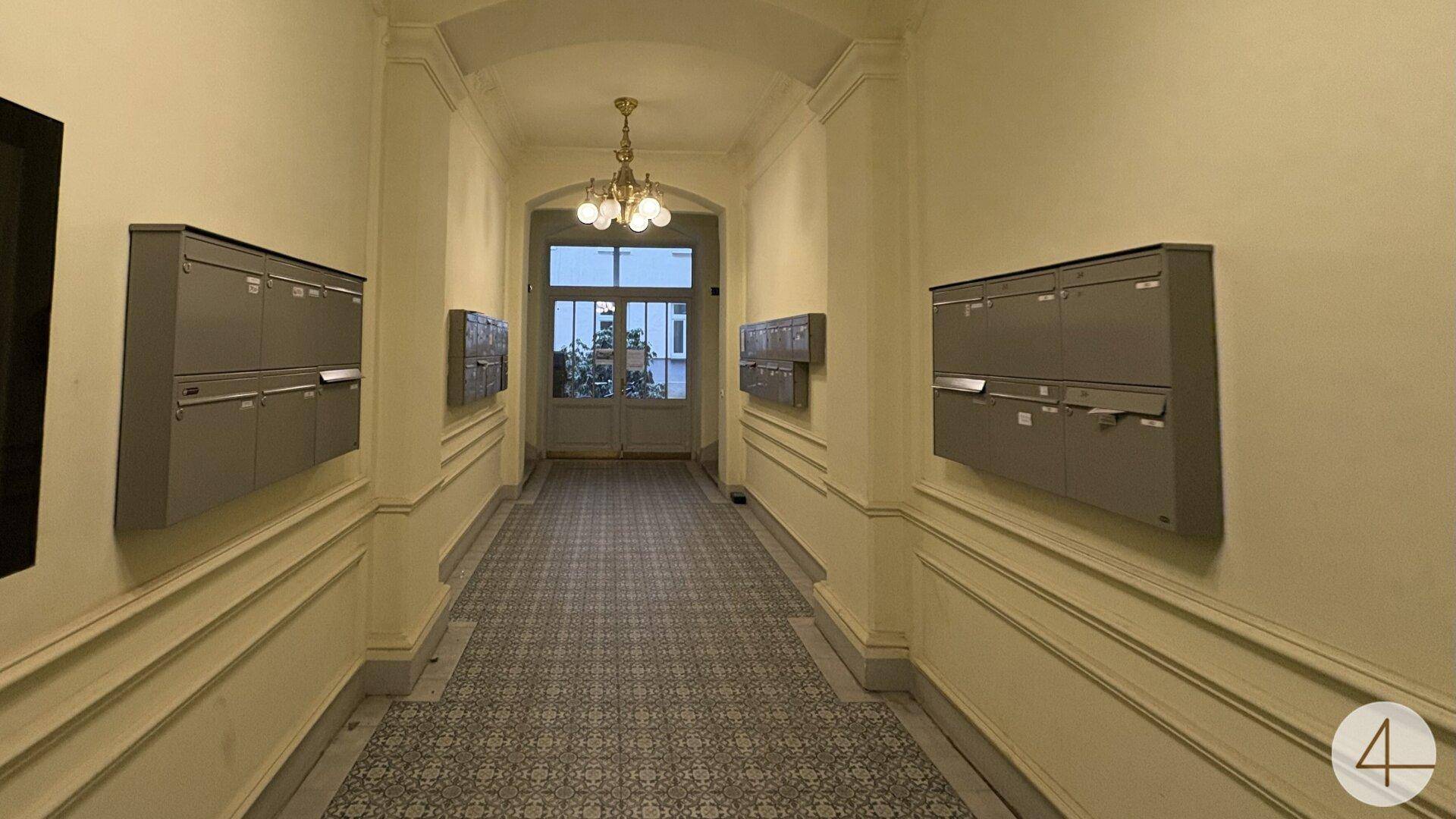 Eleganter Eingangsbereich mit gemusterten Fliesen, Stuckelementen und historischen Briefkästen.