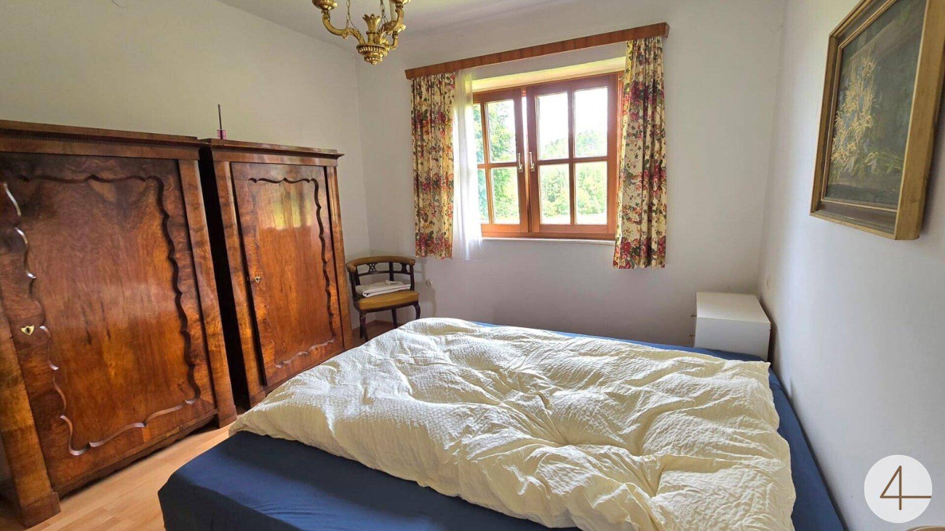 Traditionelles Schlafzimmer mit Holzbett, antiken Schränken und Blick ins Grüne.