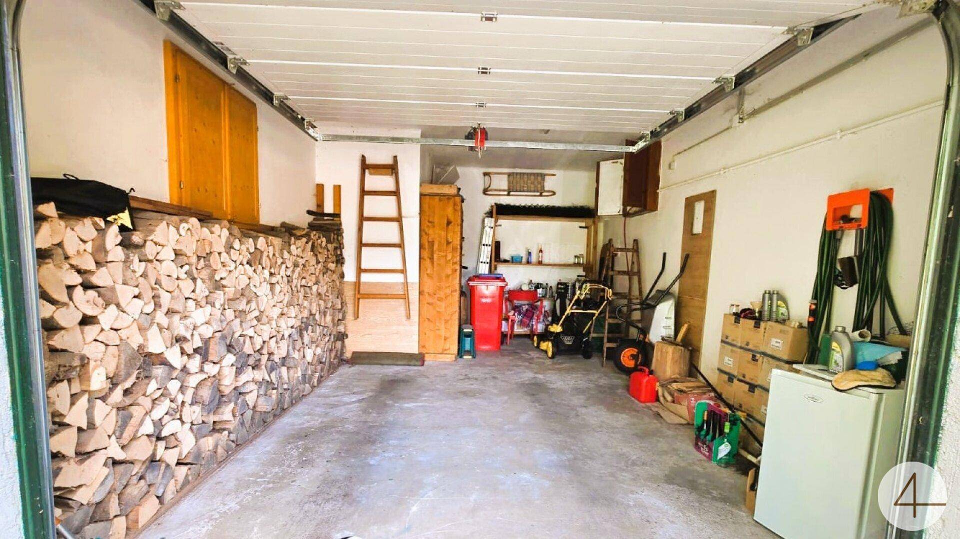 Geräumige Garage mit viel Stauraum, Brennholz und verschiedenen Gartengeräten.