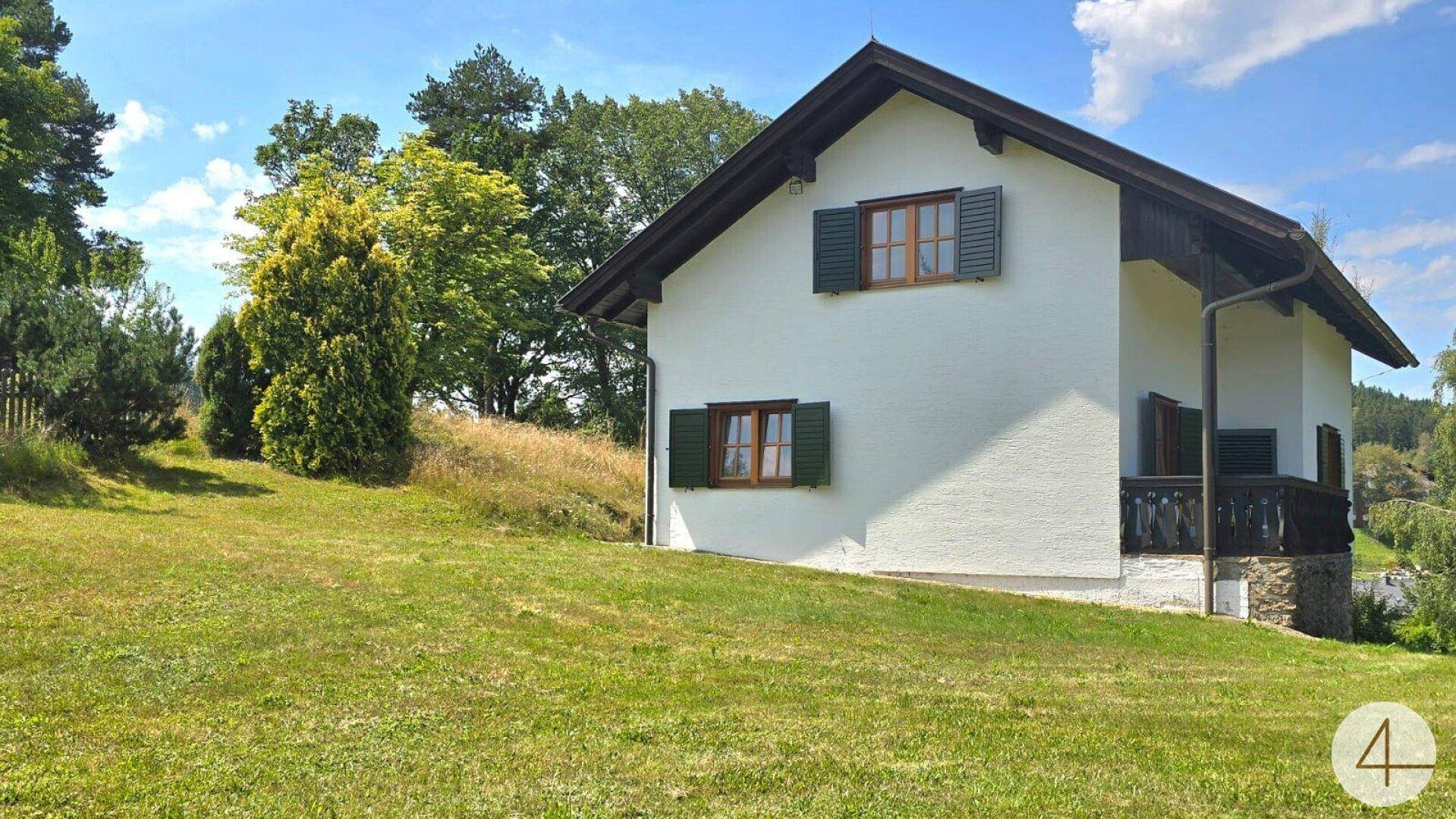 Charmantes Landhaus mit weißer Fassade, grünen Fensterläden und weitläufiger Rasenfläche.