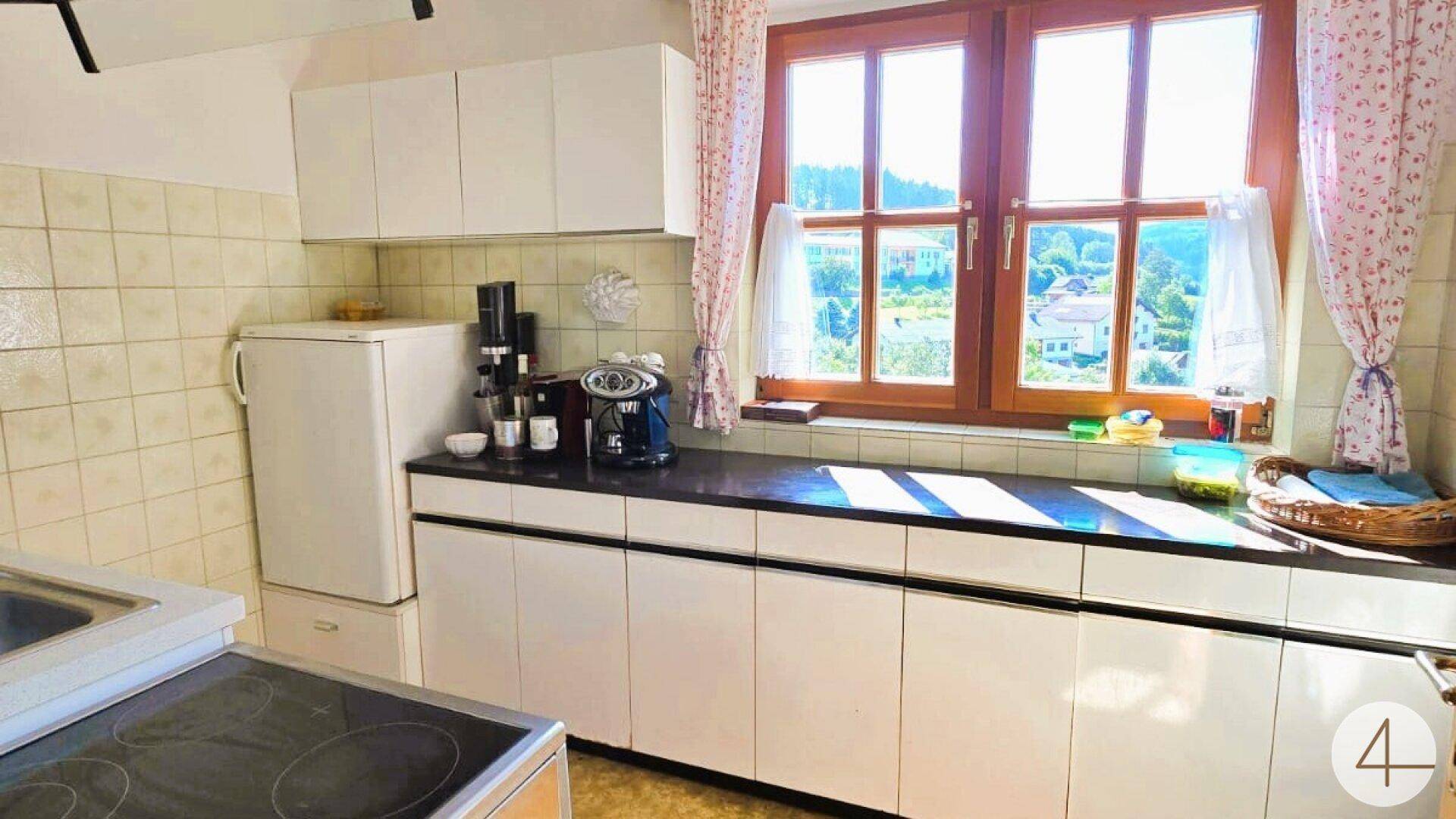 Funktionale Küche mit weißen Schränken, Fliesenrückwand und großem Fenster mit Ausblick.