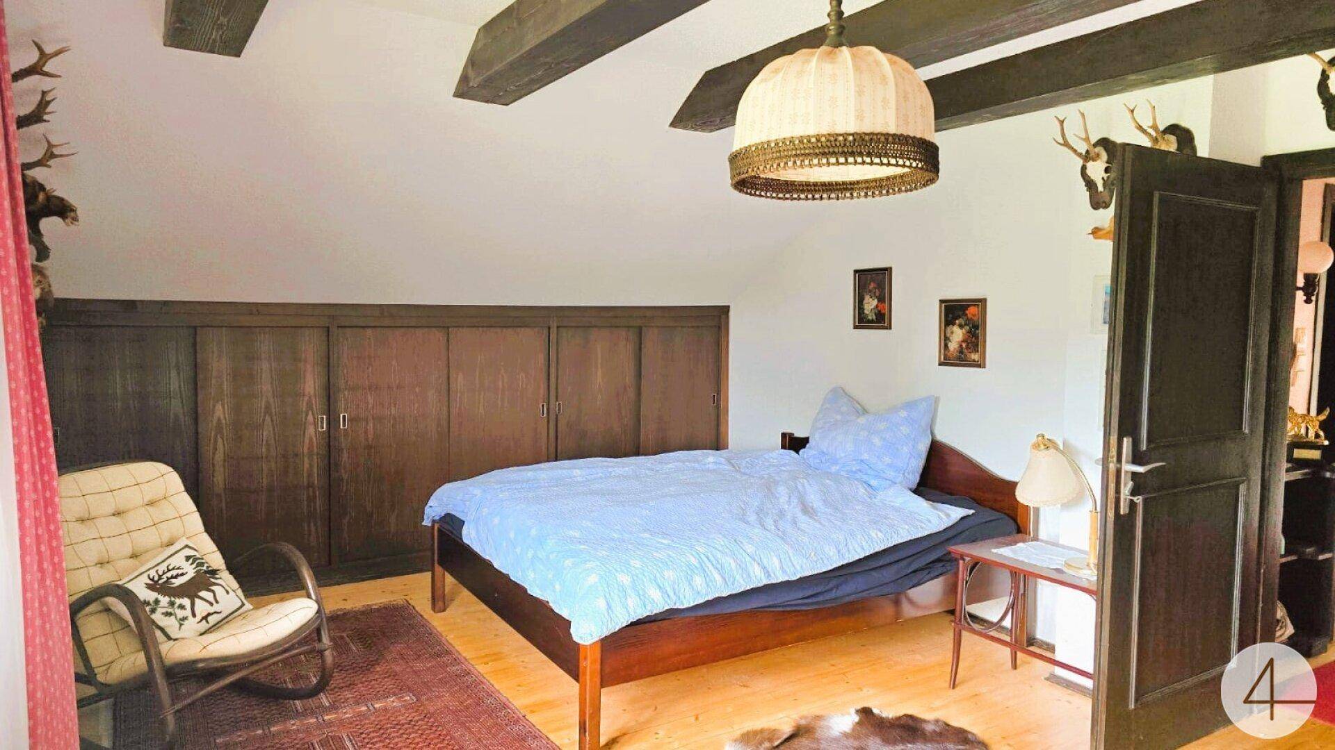 Rustikales Schlafzimmer mit Holzbalken, Dachschräge und traditioneller Hirschgeweih-Dekoration.