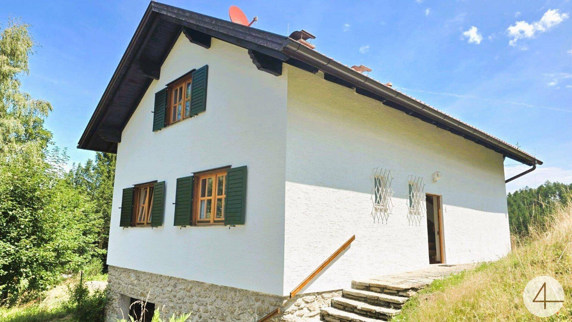 Rückseite des Landhauses mit Steintreppe, weißer Fassade und traditionellen Fensterläden.