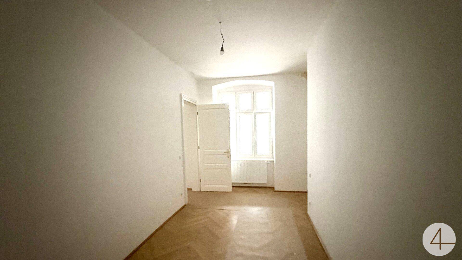Leerer Raum mit klassischem Fischgrätparkett und einem Fenster, das Tageslicht hereinlässt.
