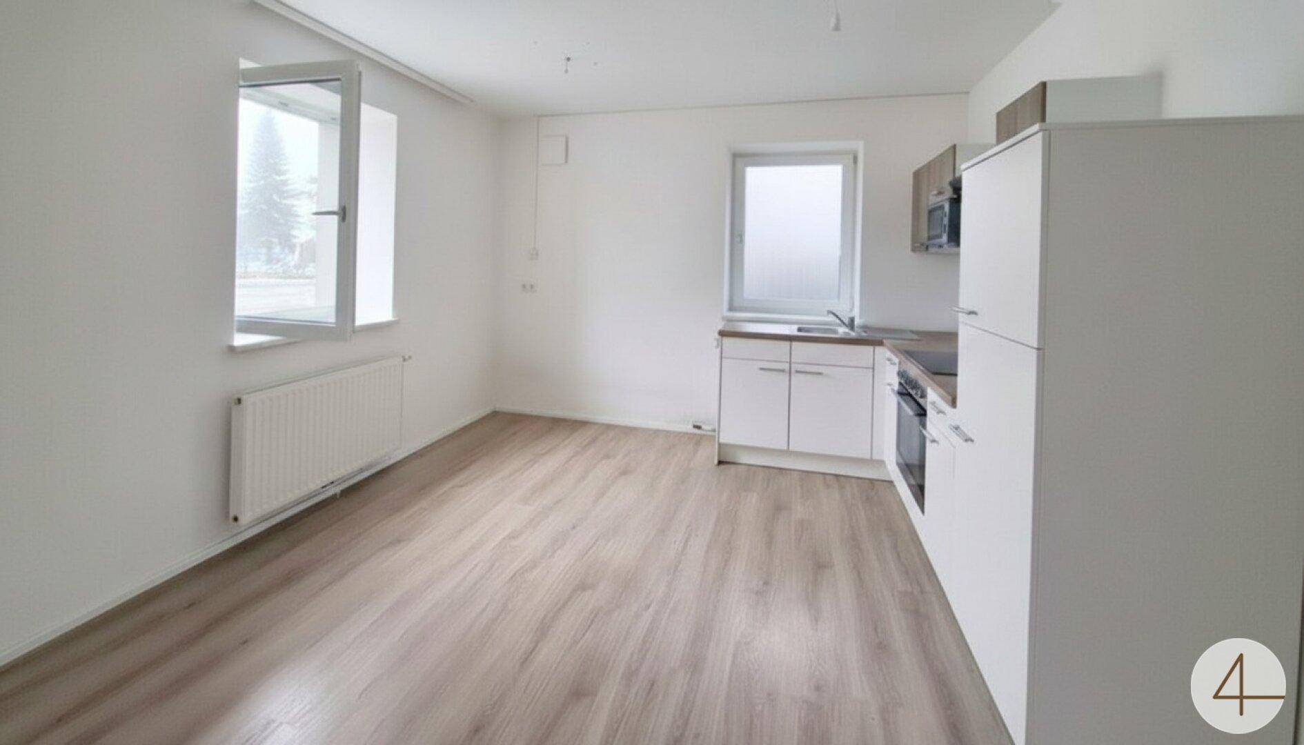 Leerer Küchenbereich mit Einbauküche, Fenster und hellem Laminatboden.