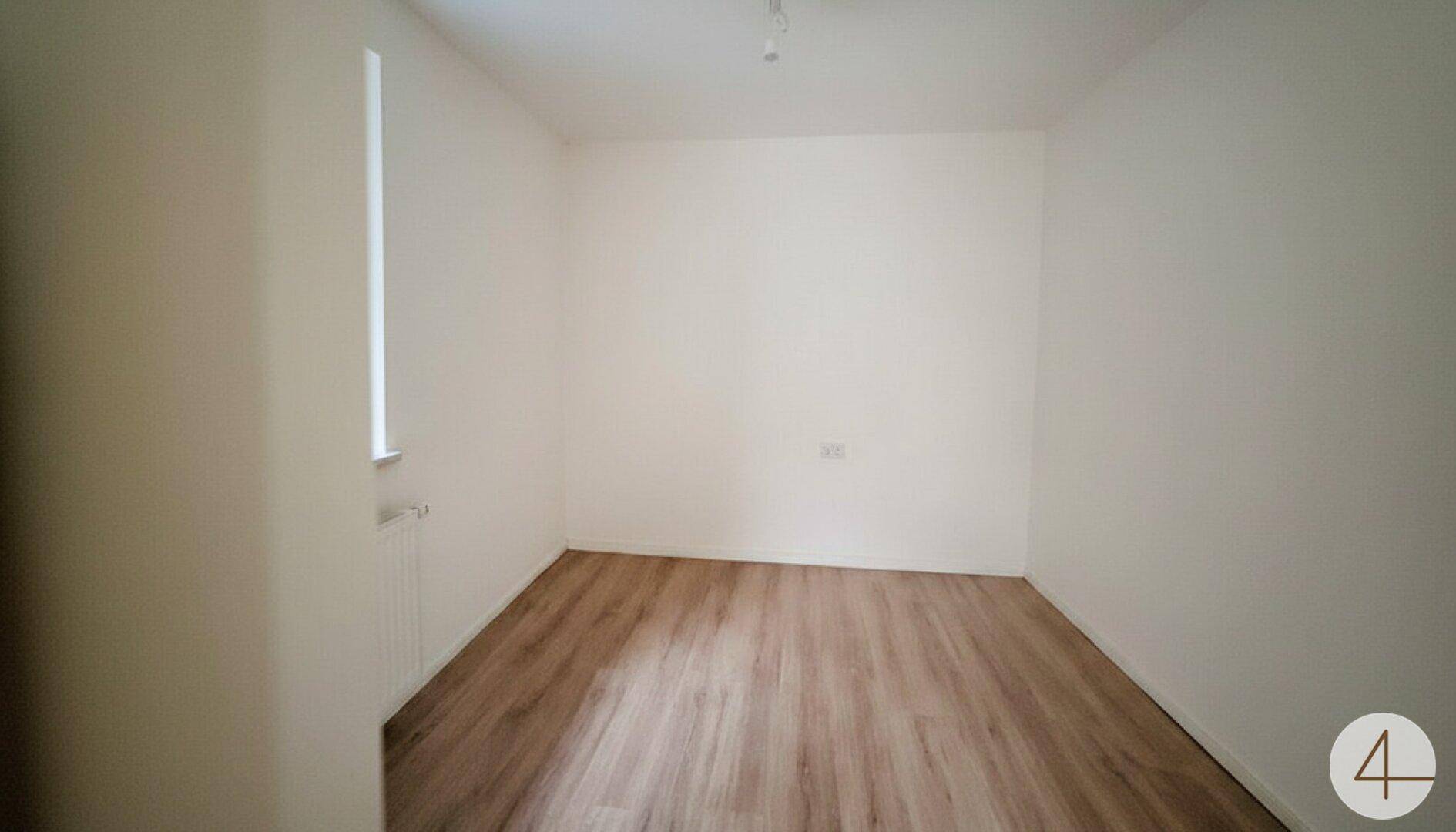 Leeres Kinderzimmer mit hellem Laminatboden, weißen Wänden und Fenster.