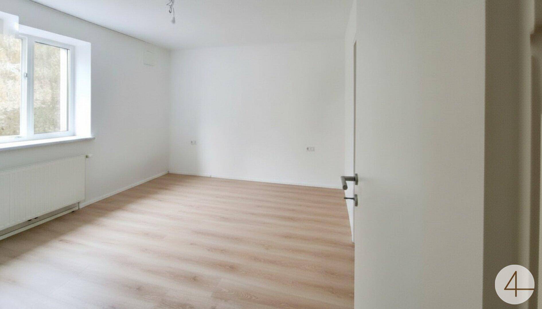 Leeres Schlafzimmer mit hellem Laminatboden, weißen Wänden und Fenster.