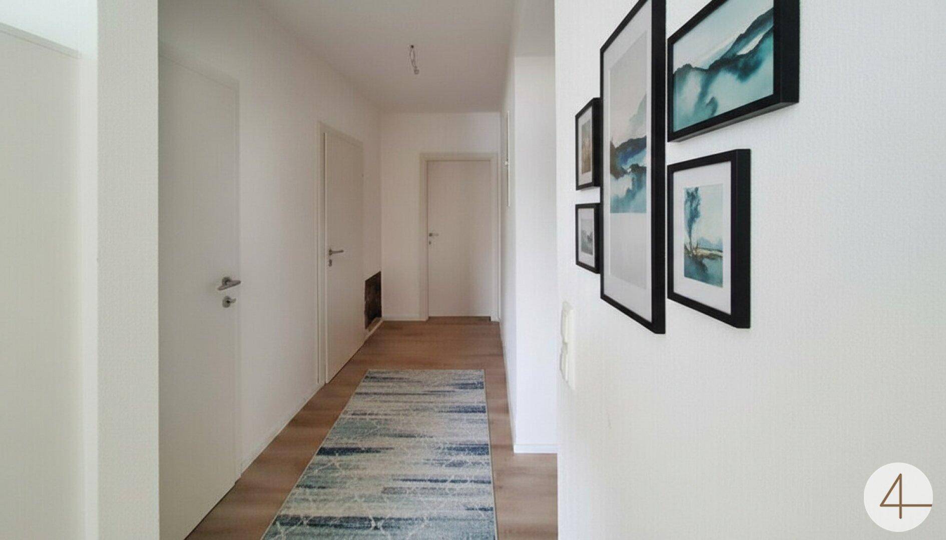 Dekorierter Flur mit Laminatboden, Teppich und modernen Bildern an der weißen Wand.