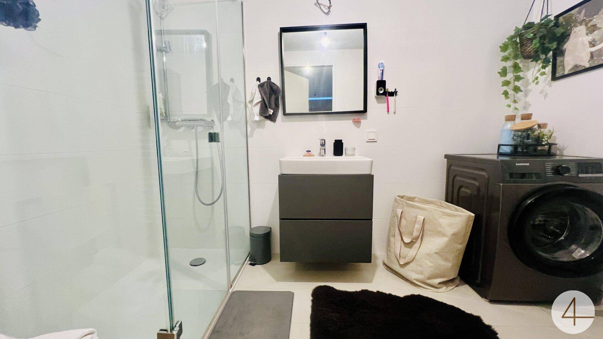 Funktionales Badezimmer mit Dusche, Waschtisch und integrierter Waschmaschine.