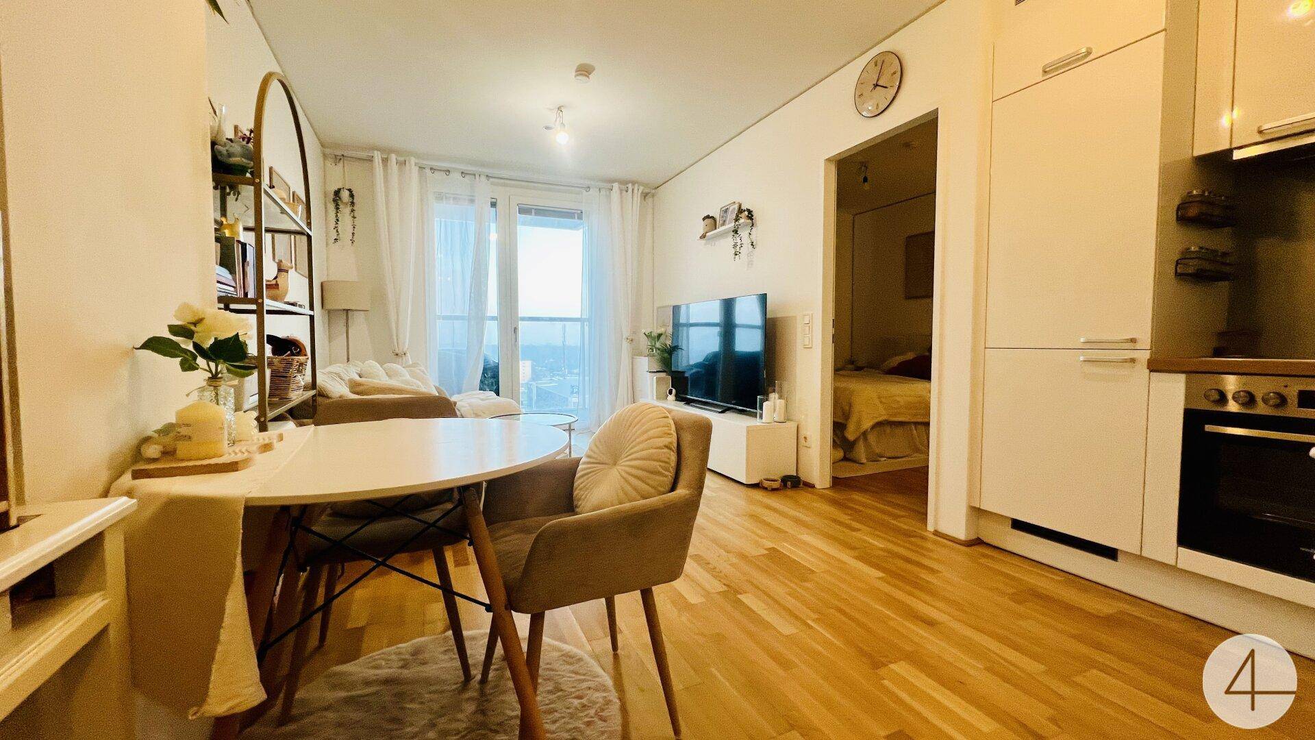 Gemütlicher Wohn- und Essbereich mit Holzboden, Zugang zum Balkon und Blick in das Schlafzimmer.