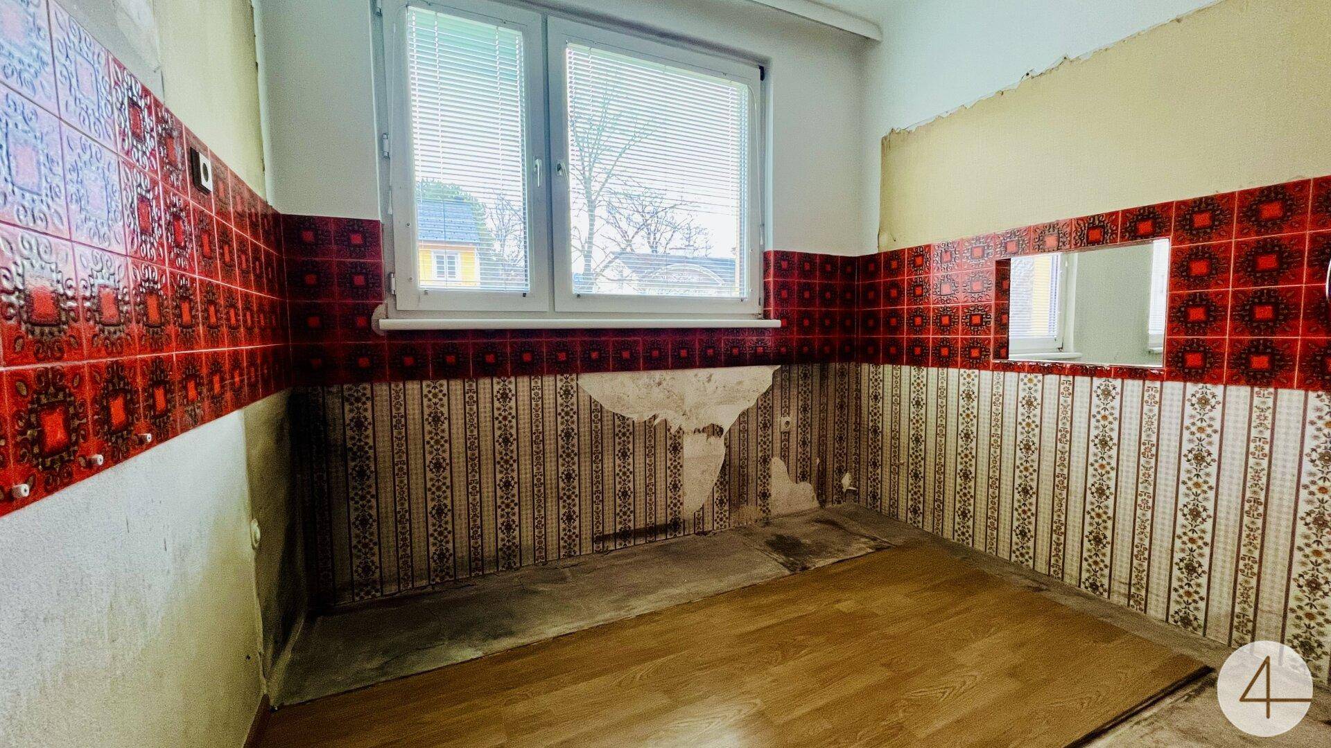 Renovierungsbedürftige Küche mit roten Fliesen, abgenutztem Boden und Fenster.