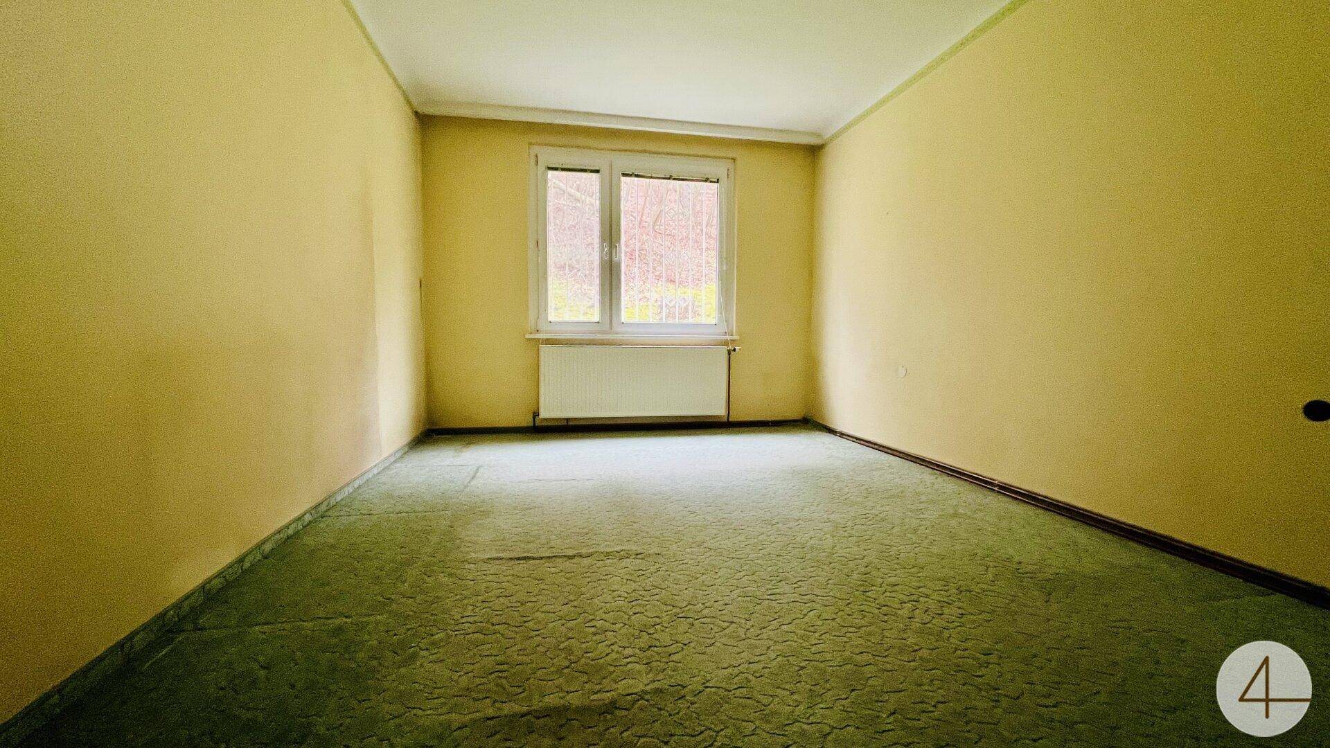 Schlafzimmer mit gelben Wänden, grünem Teppichboden und einem Fenster mit Blick ins Freie.