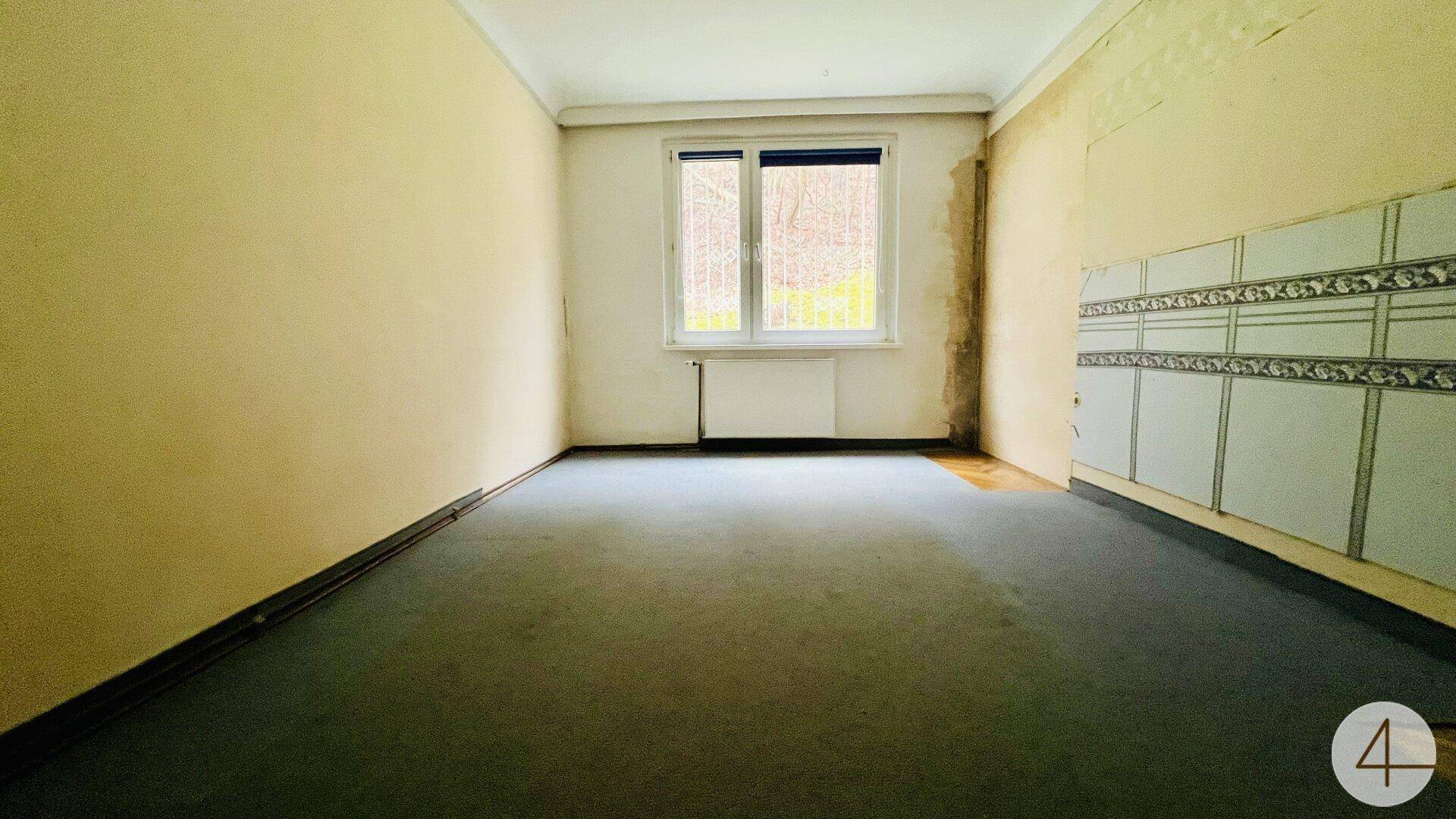 Geräumiges Zimmer mit gelben Wänden, grünem Teppichboden und einem Fenster.