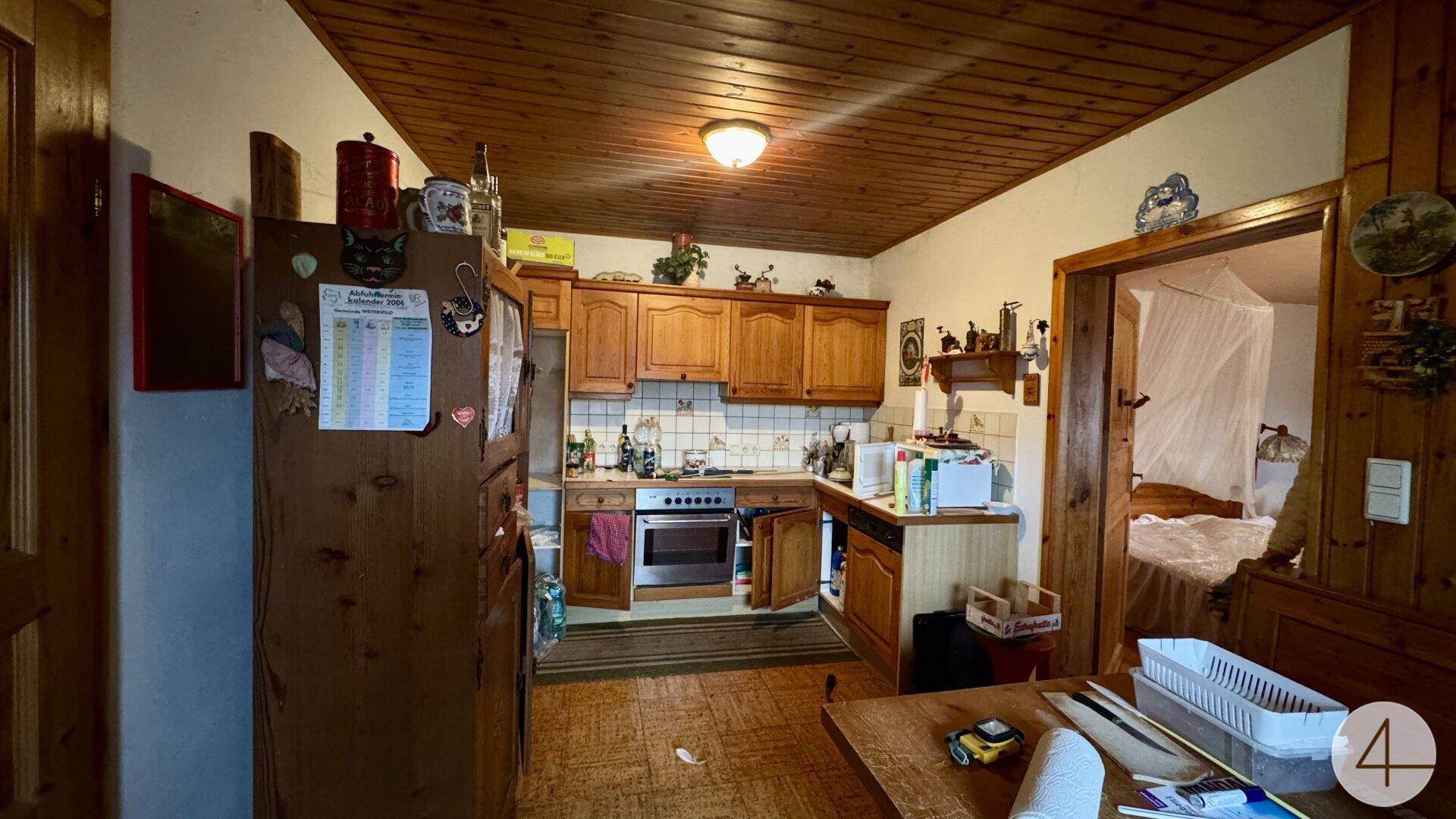 Rustikale Küche mit Holzschränken, integrierten Geräten und Blick in ein angrenzendes Schlafzimmer.
