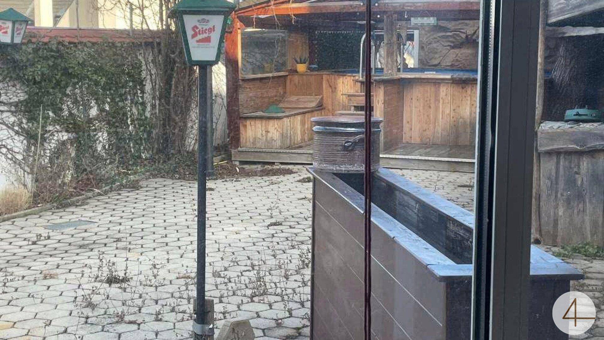 Blick aus einem Fenster auf den gepflasterten Außenbereich mit Holzstrukturen und einer Laterne.