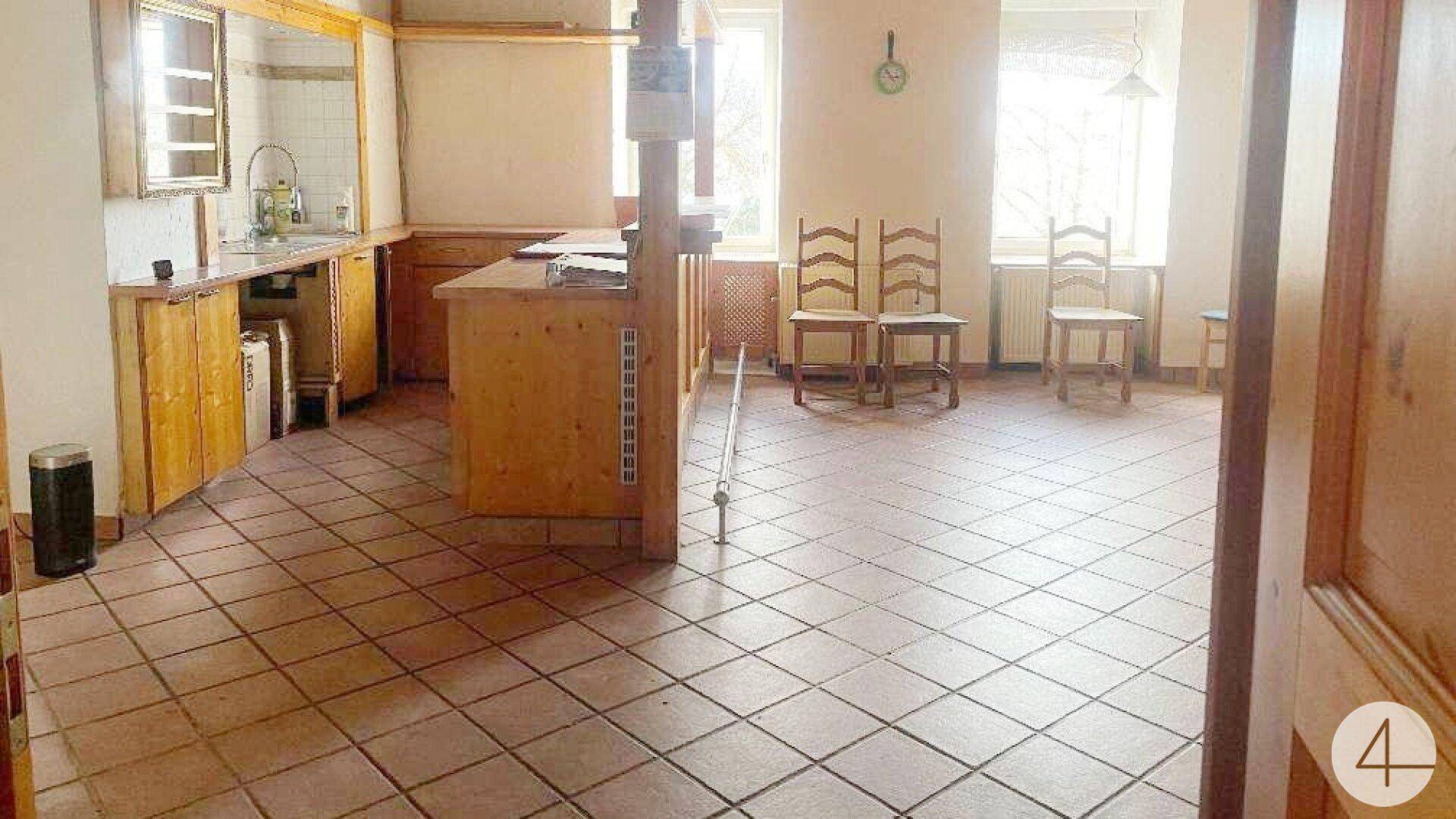 Geräumige Küche mit Holzschränken, Fliesenboden und einem offenen Bereich, der als Esszimmer genutzt werden könnte.
