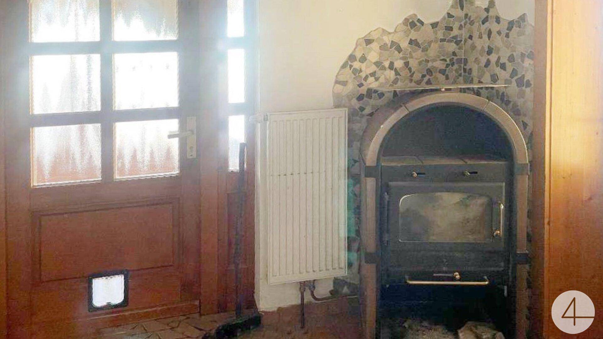 Eingangsbereich mit Holztür, Heizkörper und einem rustikalen Kaminofen.