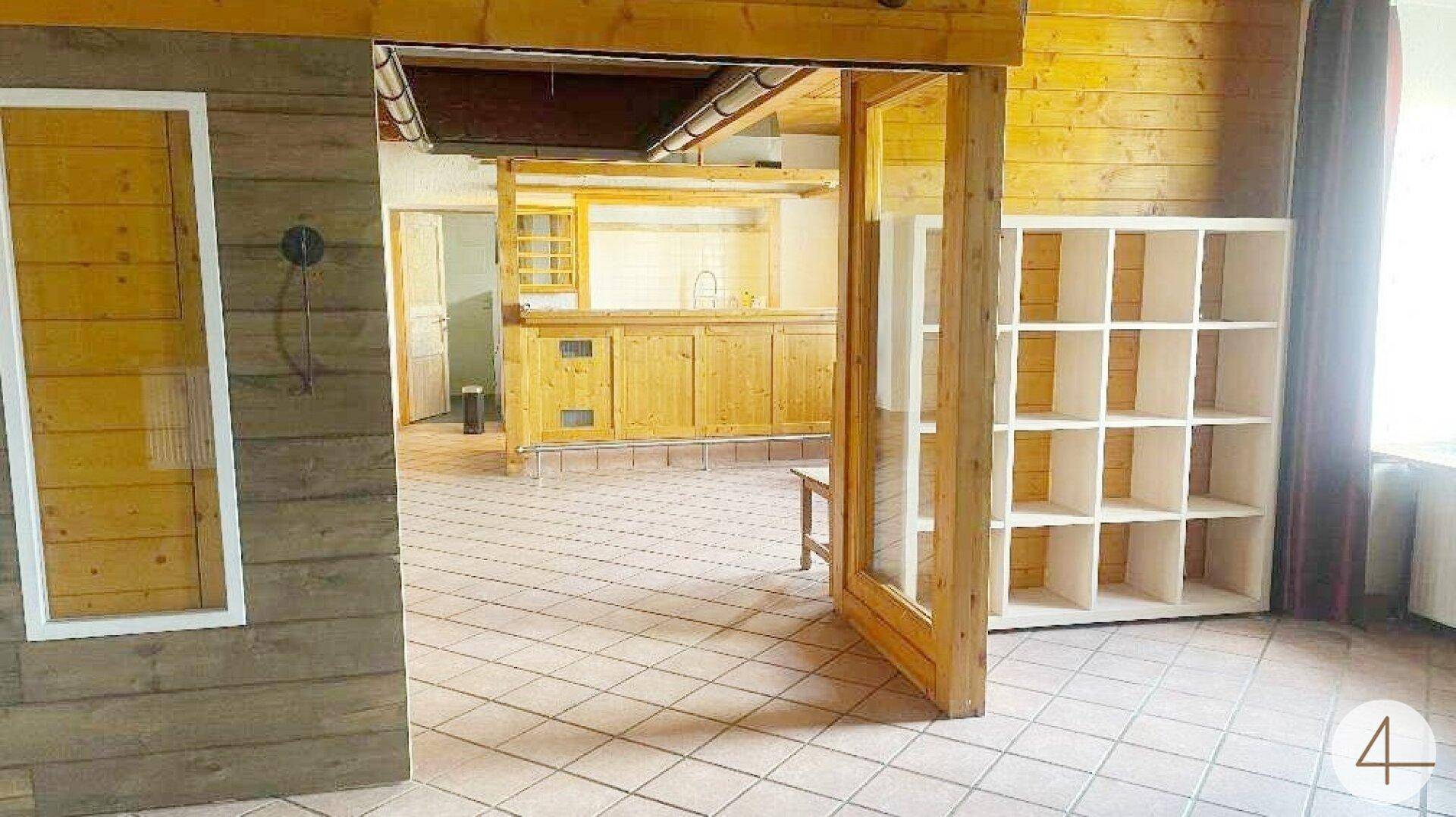 Heller Durchgangsbereich mit Holzwänden und Blick in eine Küche mit Holzmöbeln und Fliesenboden.