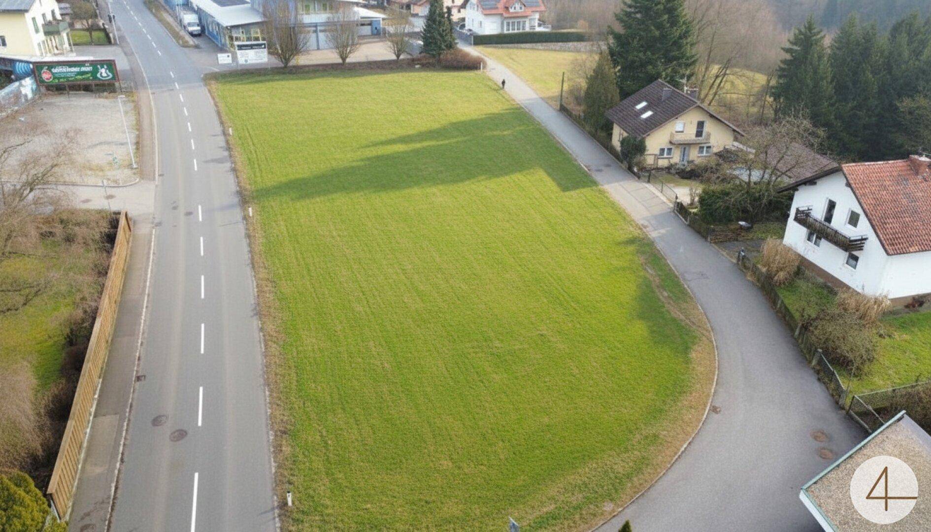 Luftaufnahme eines großen grünen Grundstücks an einer Straßengabelung, umgeben von Wohnbebauung.