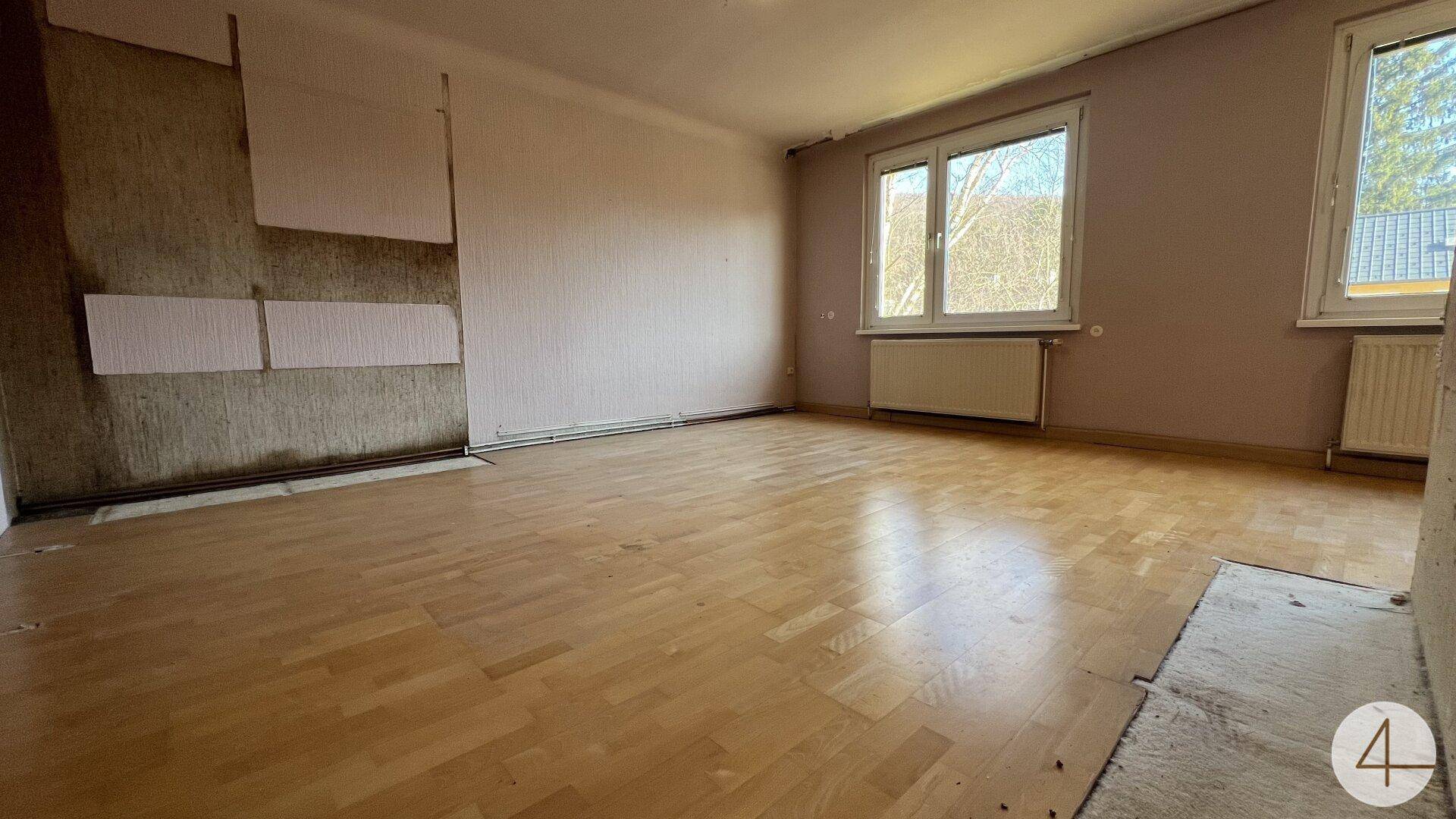Leeres Zimmer mit Parkettboden und abgenutzten Wänden, das eine Modernisierung benötigt.