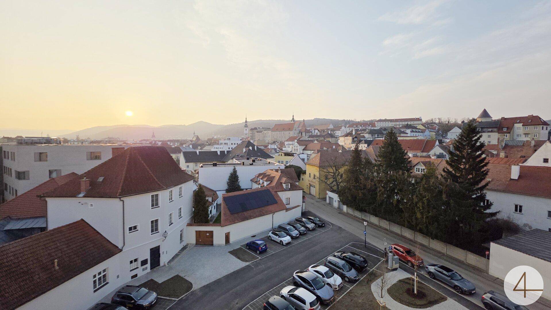 Panoramablick über eine charmante Stadt mit roten Dächern und umliegenden Hügeln bei Sonnenuntergang.